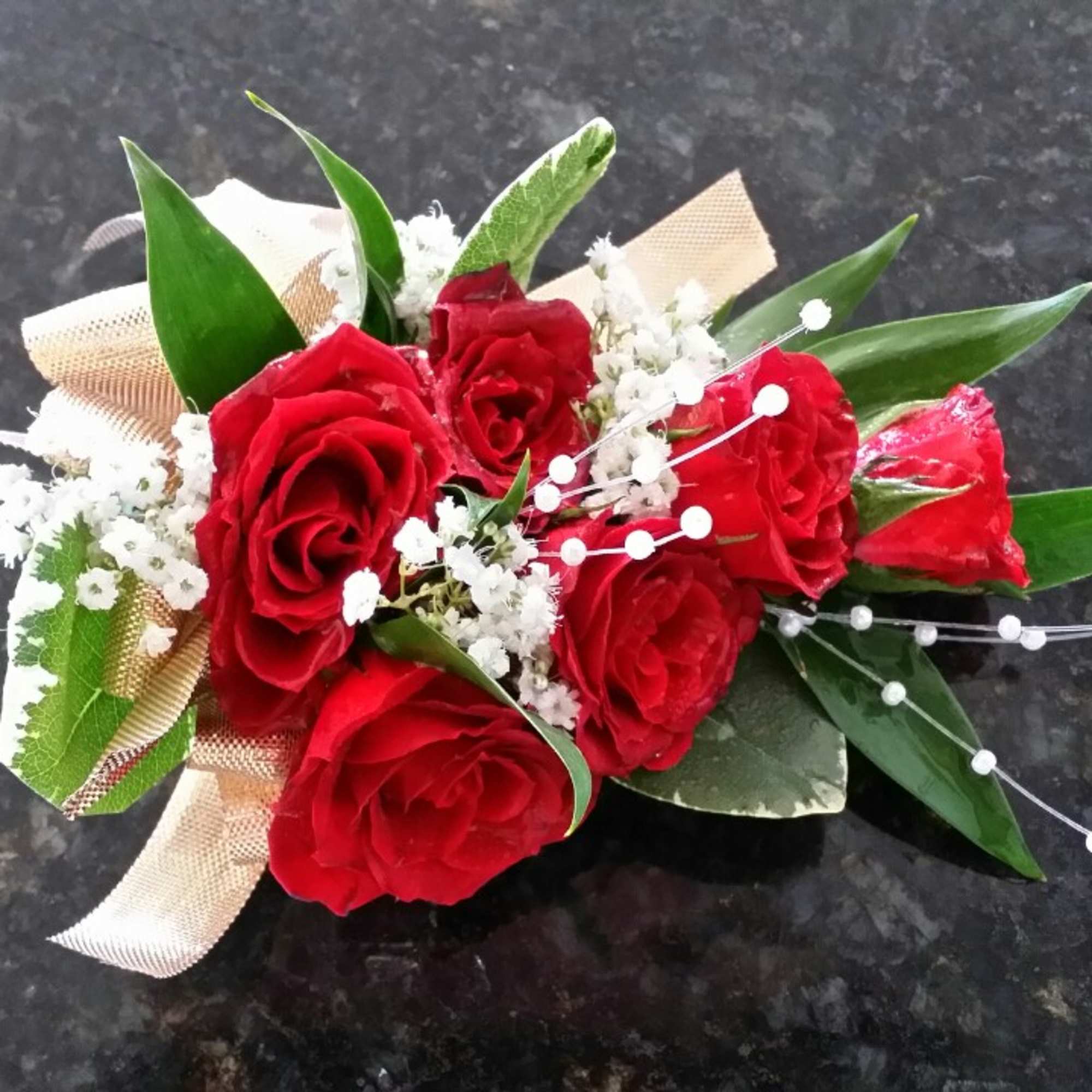 Red rose bouquet with white filler and ribbon on a dark surface