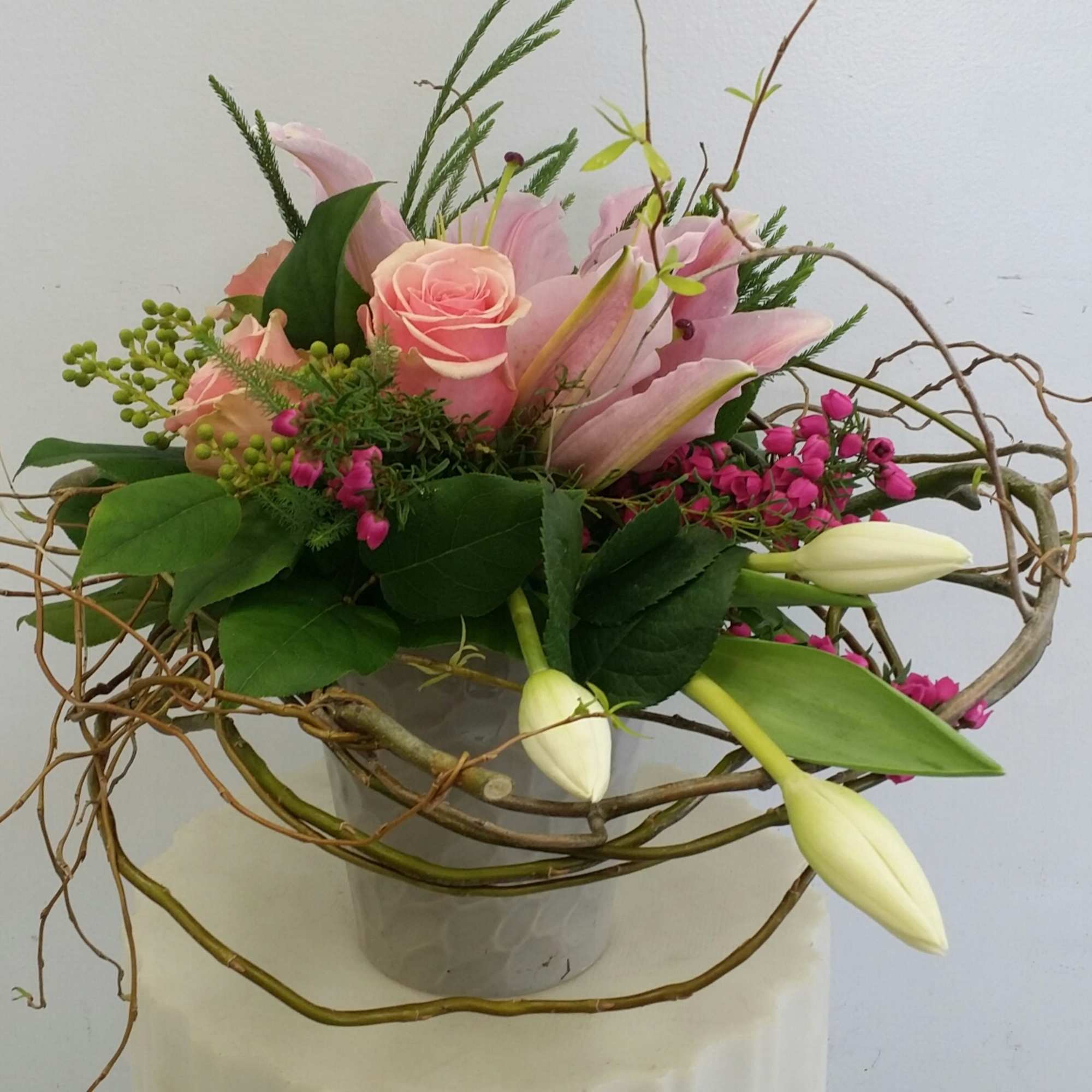 Pink roses and lilies in a glass vase with curly branches