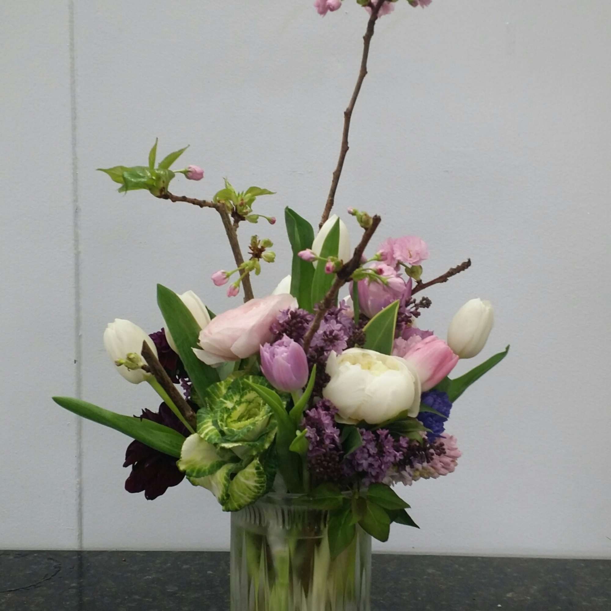 Pink and white tulips with blossoms in a clear glass vase
