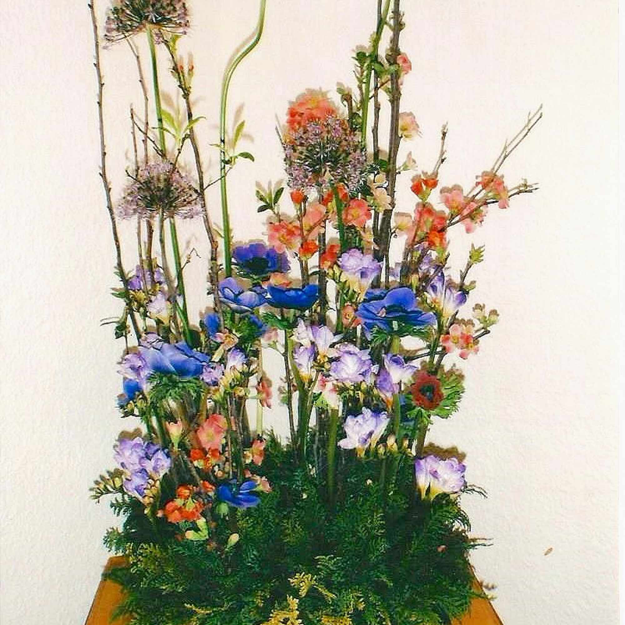 Tall mixed floral arrangement with blue, purple, and orange blooms on a wooden pedestal