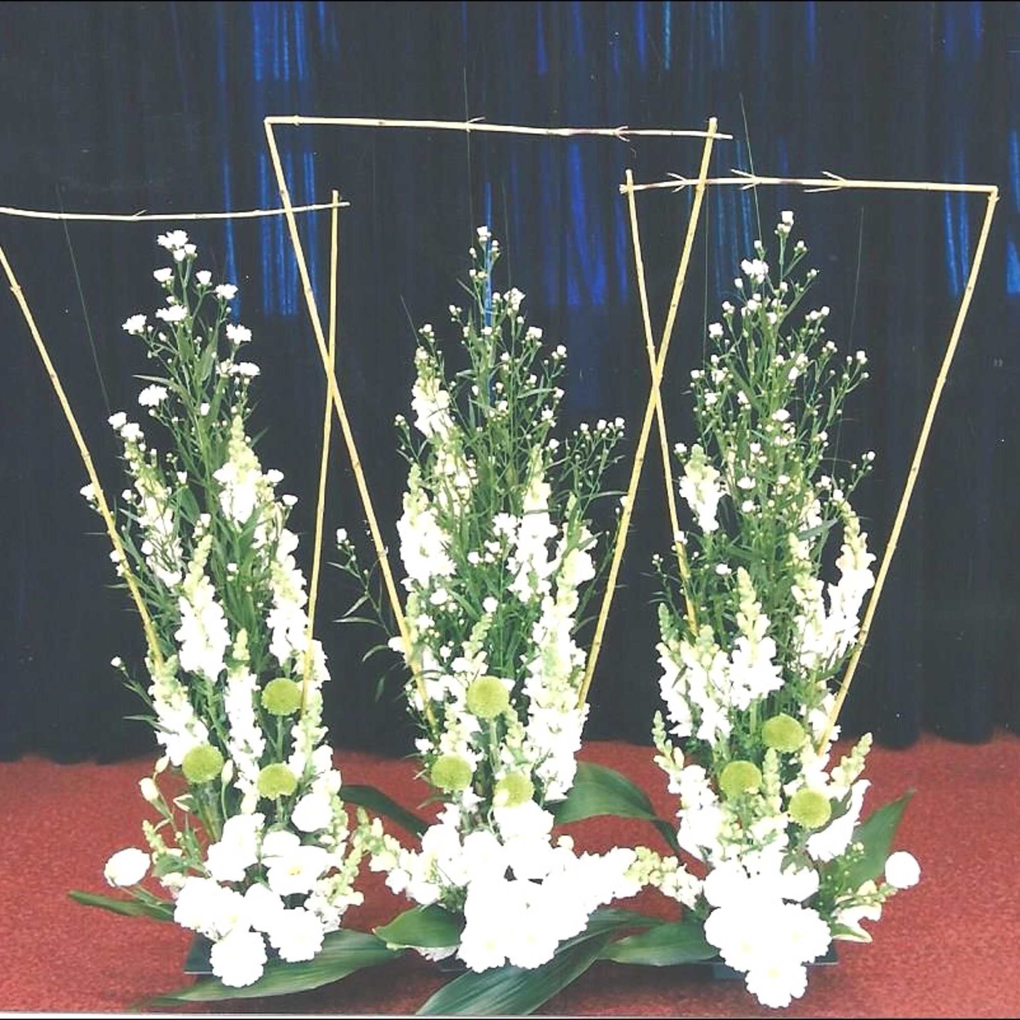 Three tall white floral arrangements with gold geometric frames