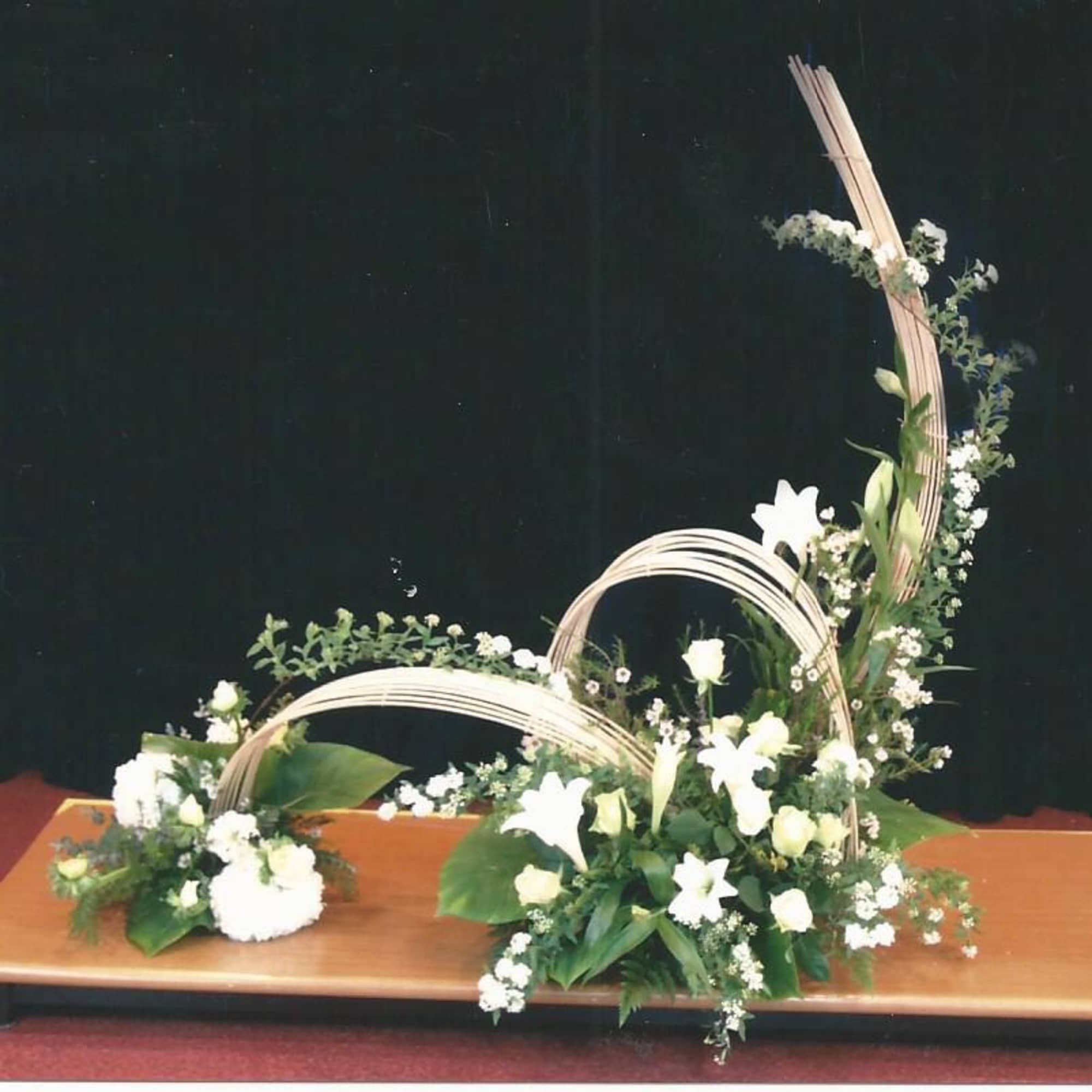 White floral arrangement with arched decorative branches on a low platform