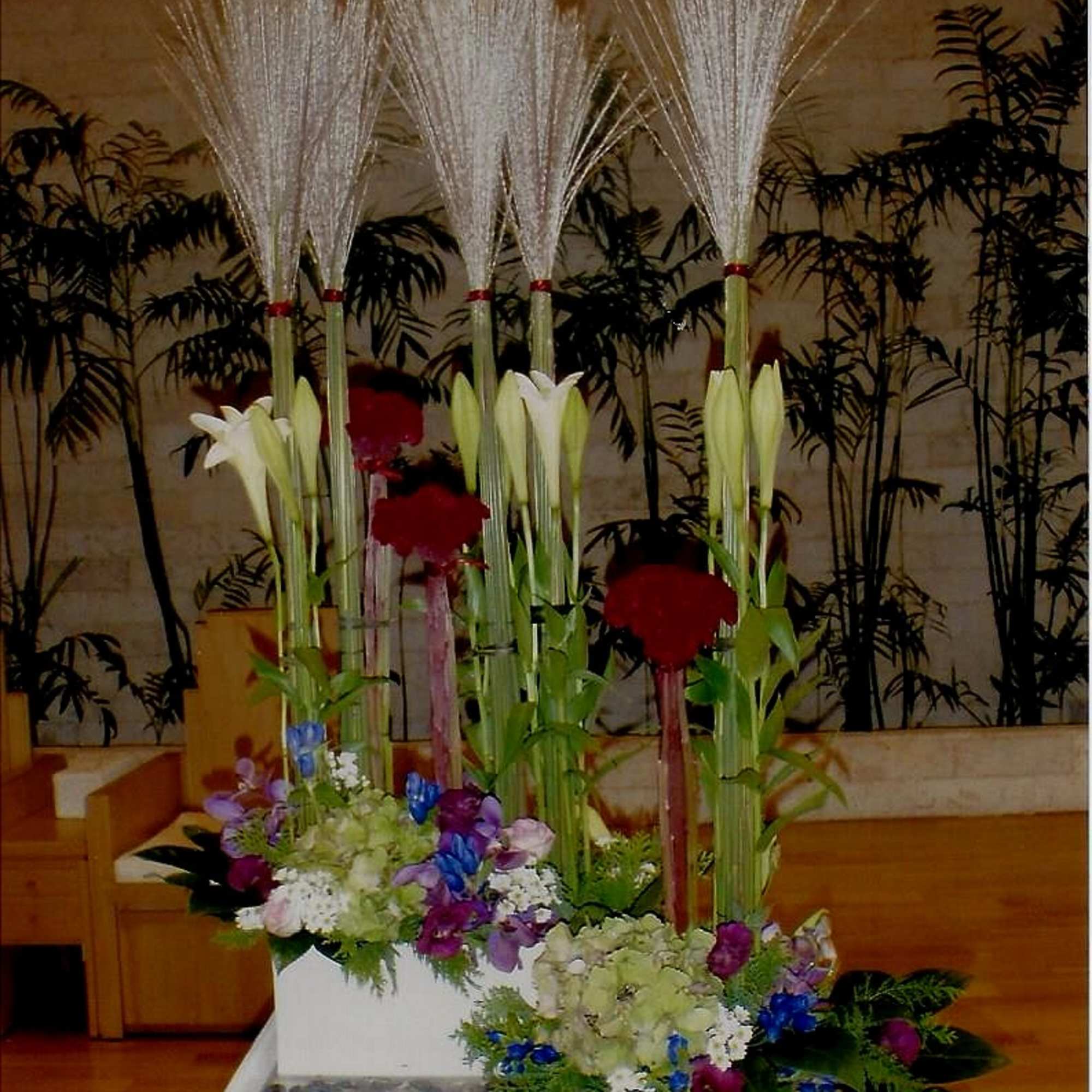 Tall floral arrangement with white lilies and red blooms in a white container