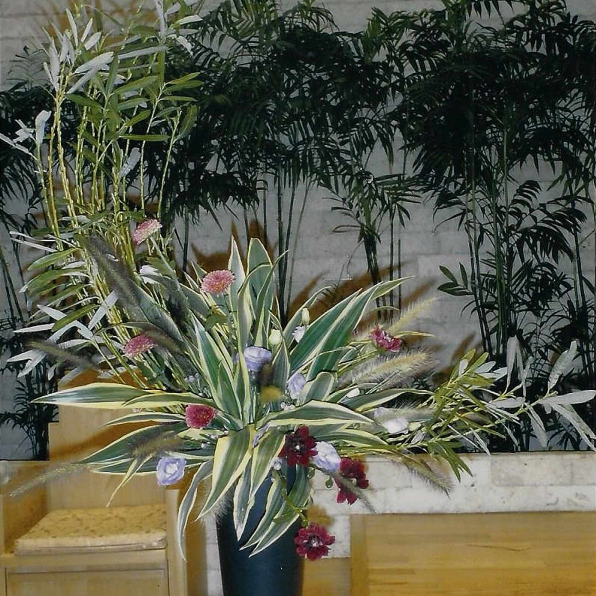Tall tropical arrangement with variegated leaves and small pink flowers in a dark vase