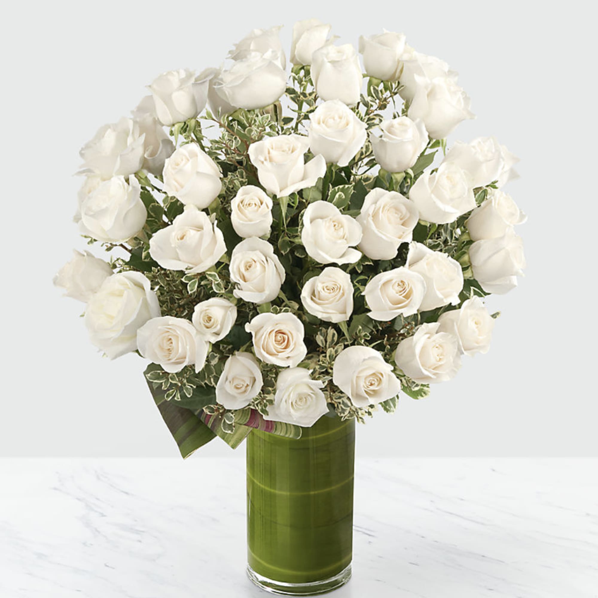 White roses arranged in a tall green glass vase