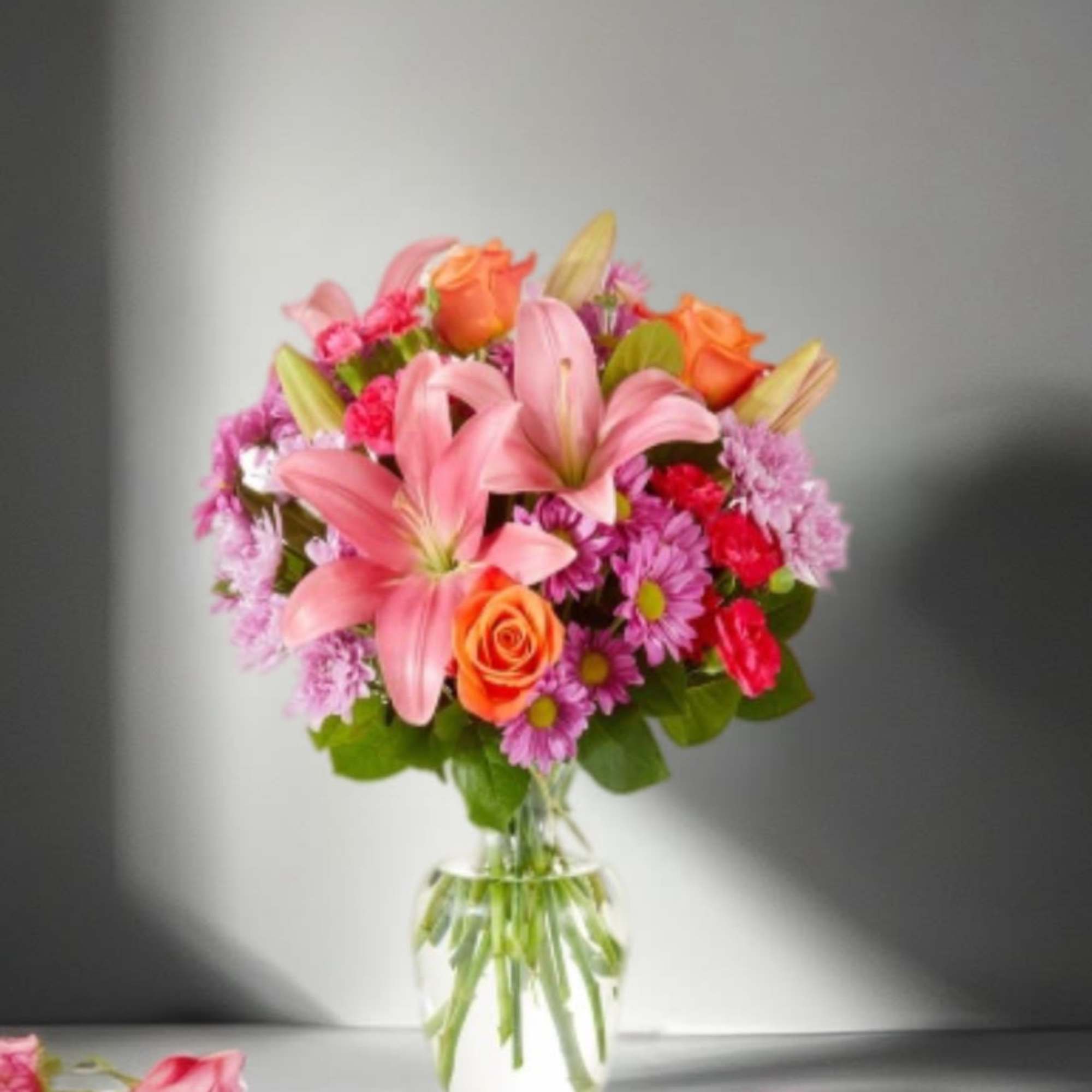 Pink lilies and mixed roses in a clear glass vase
