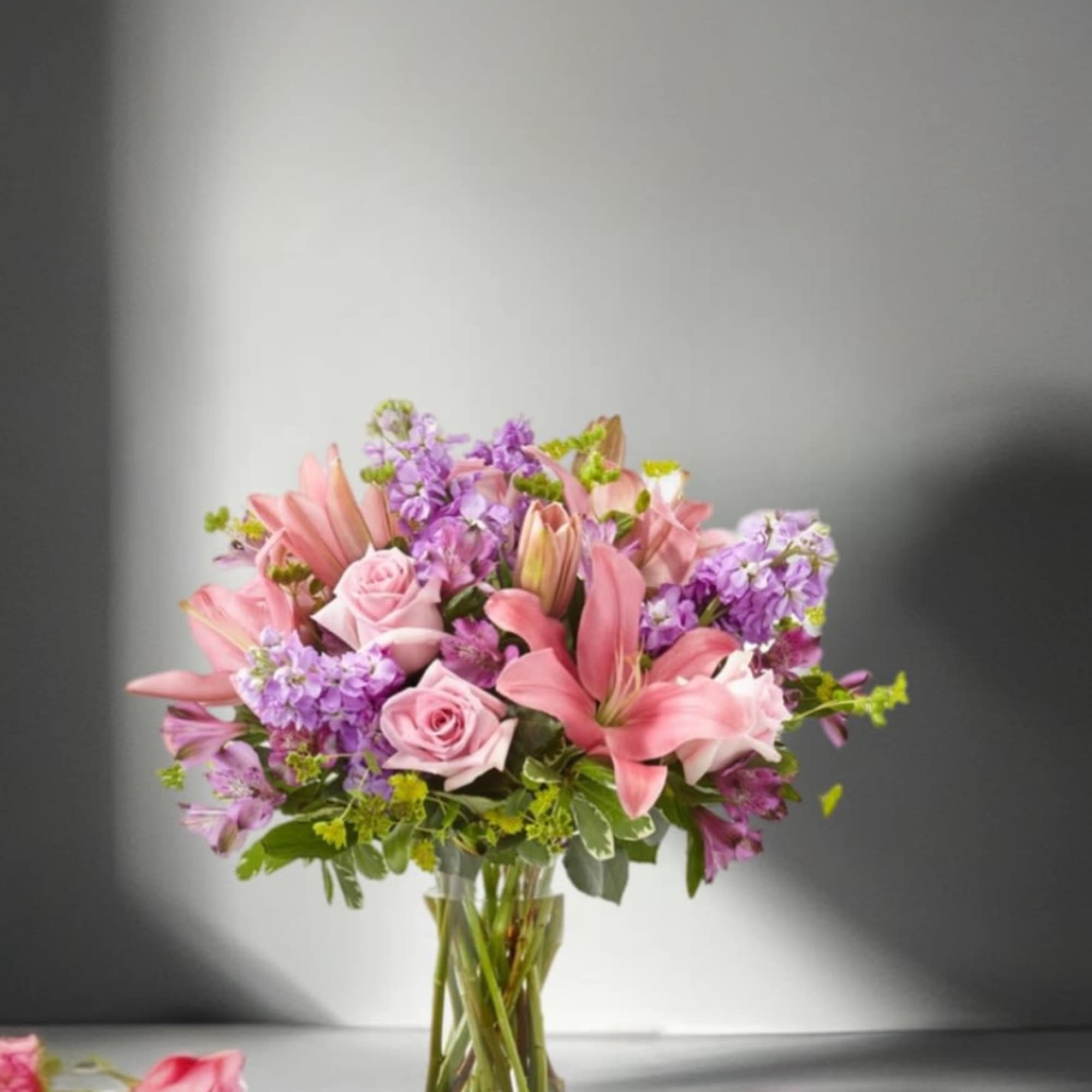 Pink lilies and roses arranged in a clear glass vase