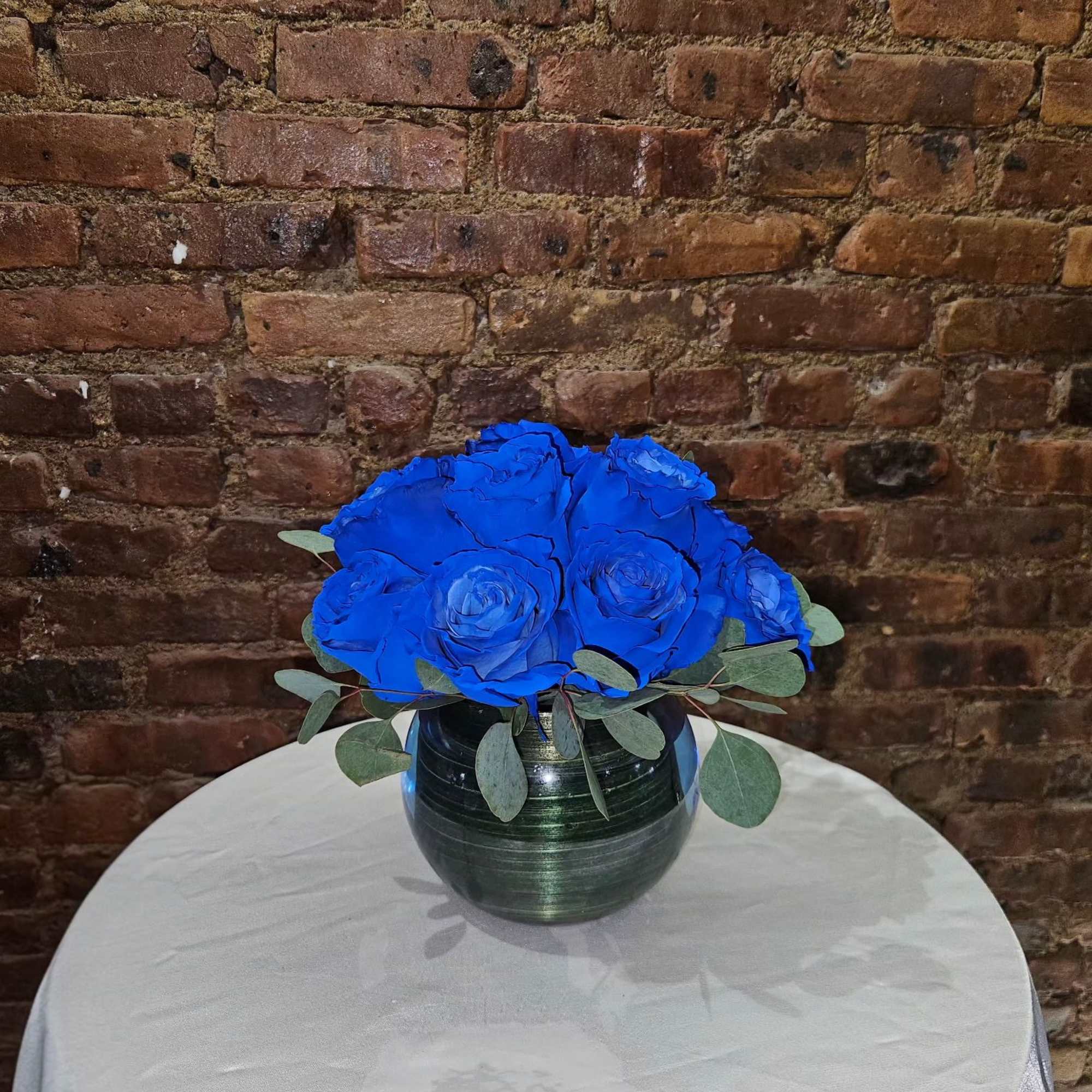 Blue rose bouquet in a dark glass vase on a round table