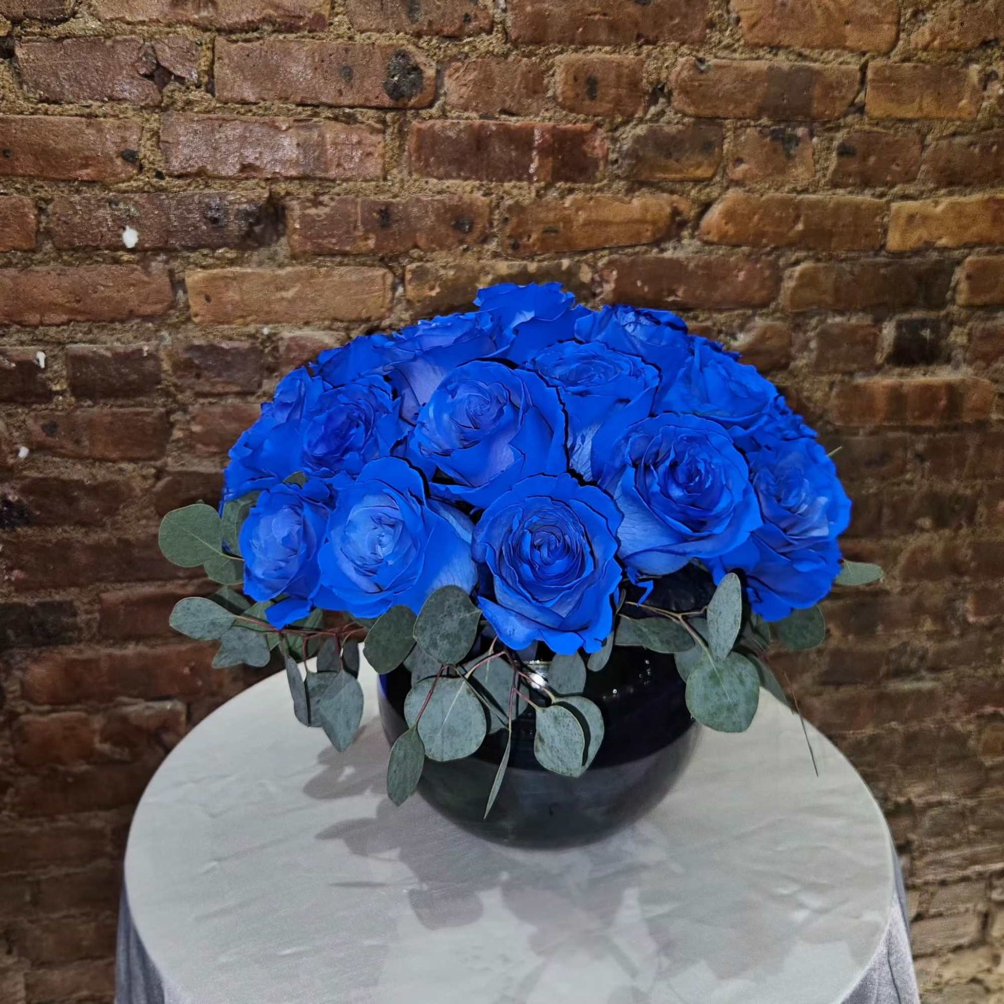 Blue roses arranged in a black vase with eucalyptus leaves