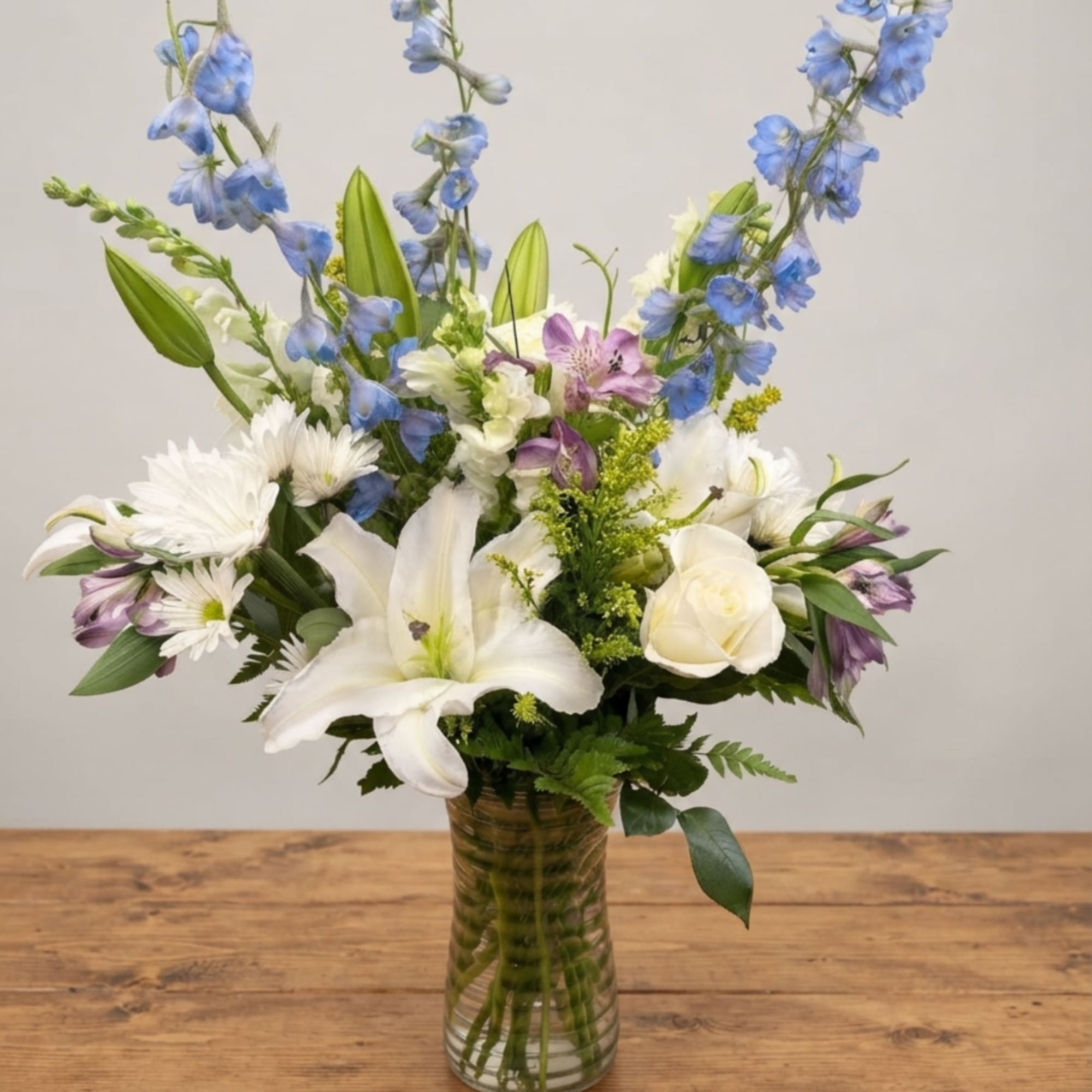 White lilies, roses, and blue delphinium in a glass vase