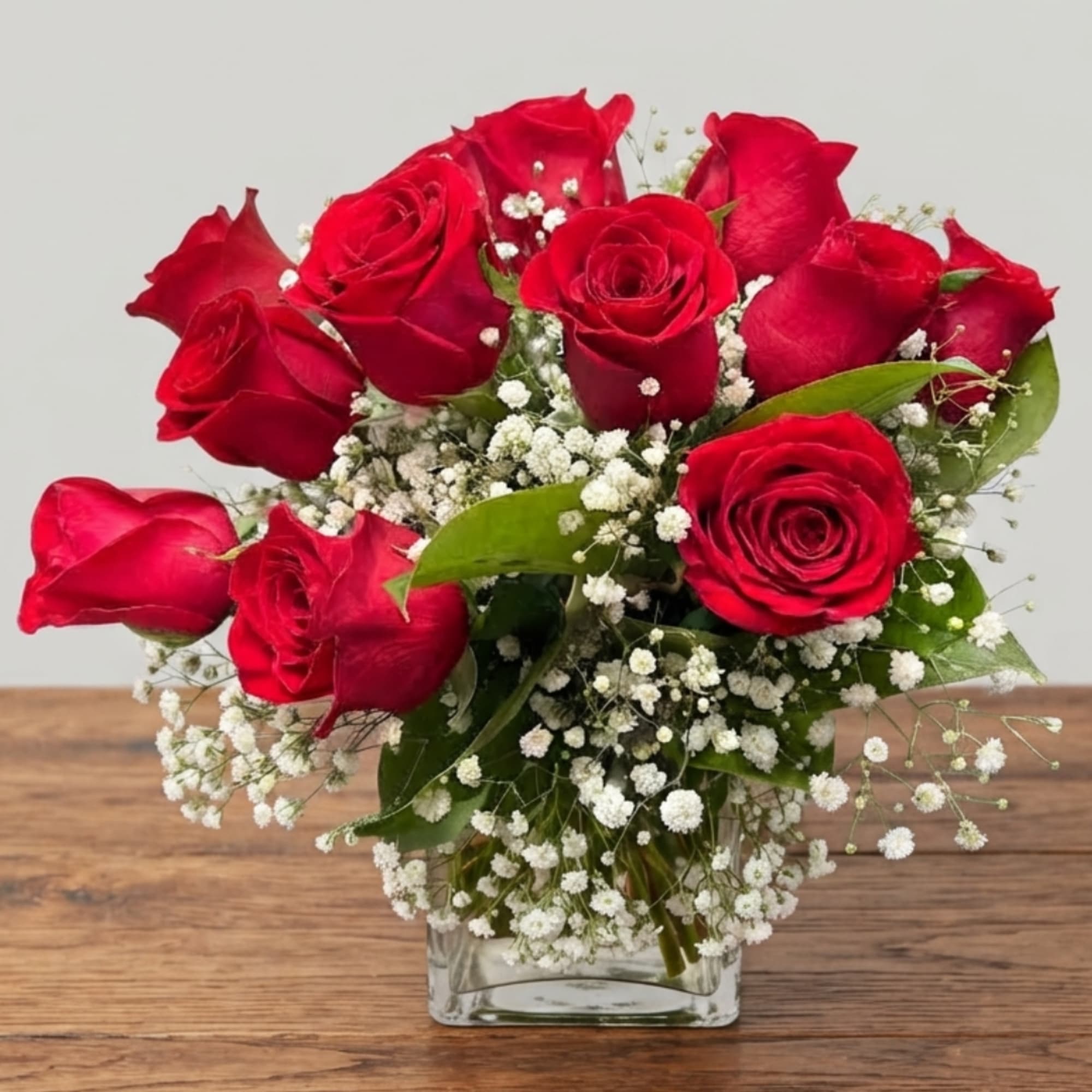 Red roses arranged in a clear square vase with white baby's breath