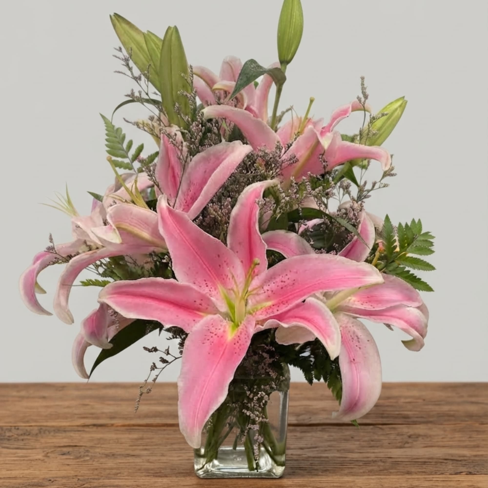 Pink lilies arranged in a clear glass vase with mixed greenery
