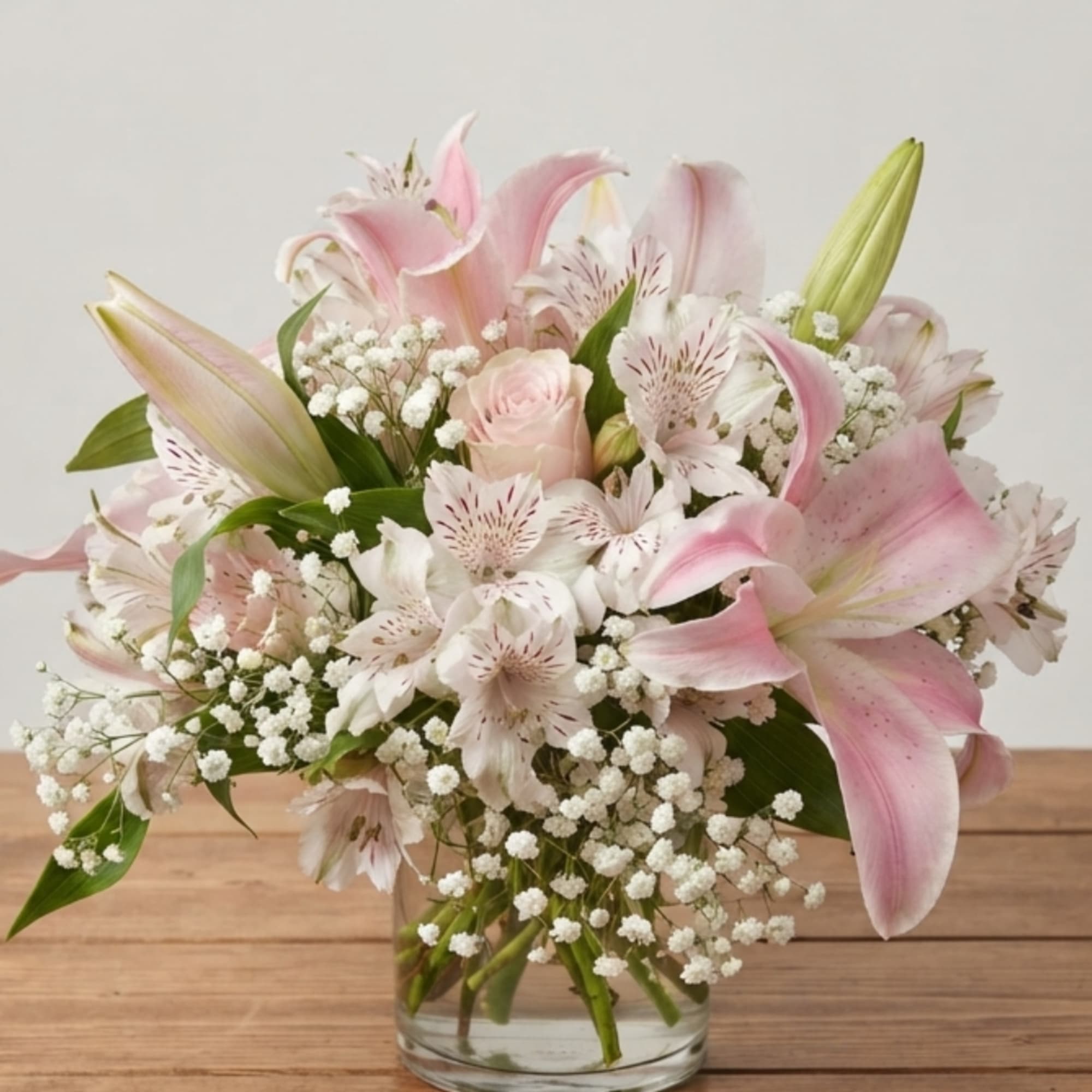 Pink lilies and white filler flowers arranged in a clear glass vase
