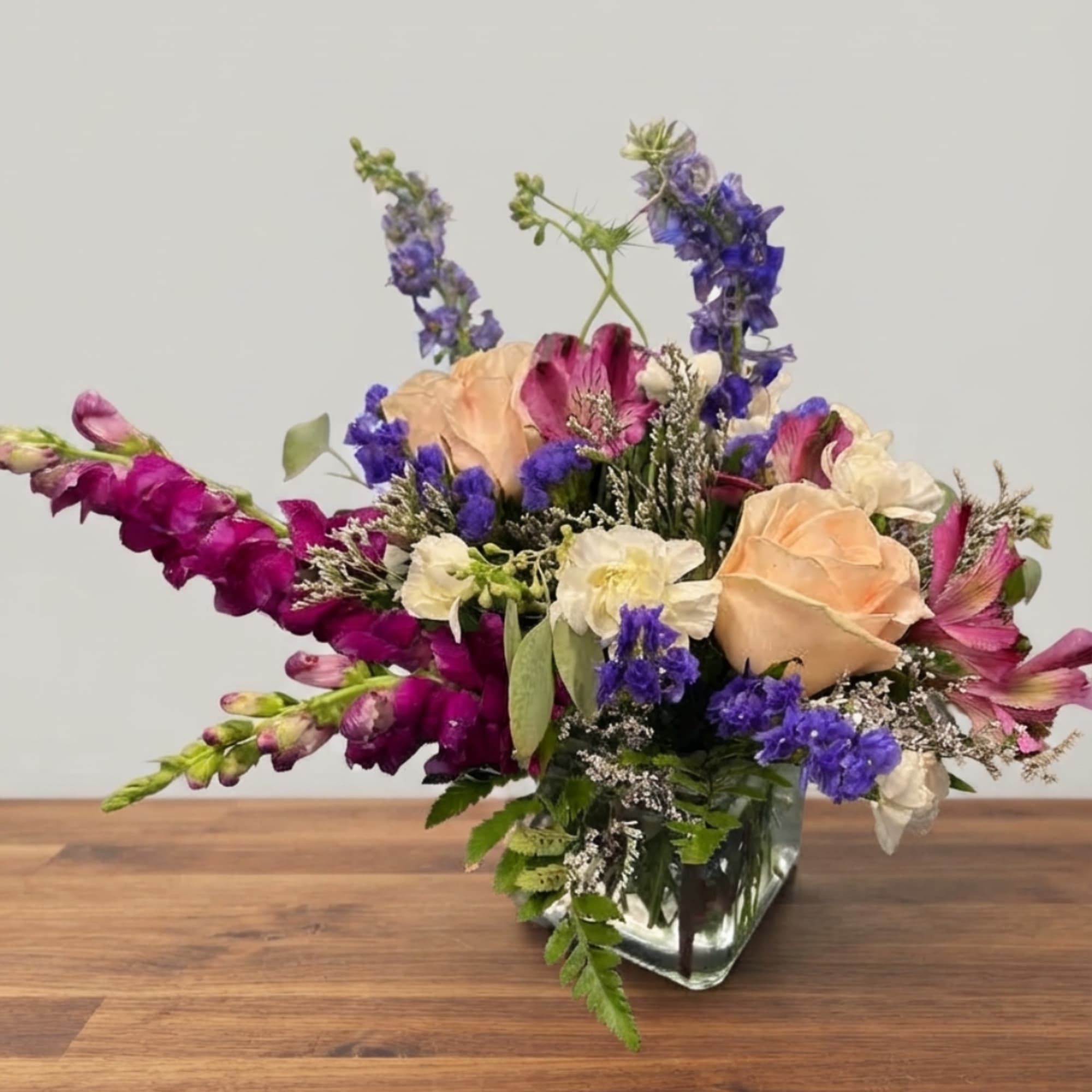 Mixed bouquet of peach roses, purple blooms, and white flowers in a glass vase