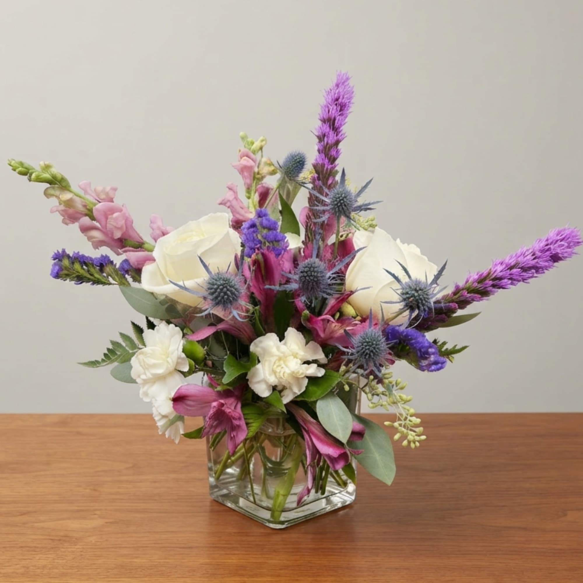 Mixed bouquet of white, pink, and purple flowers in a clear square vase