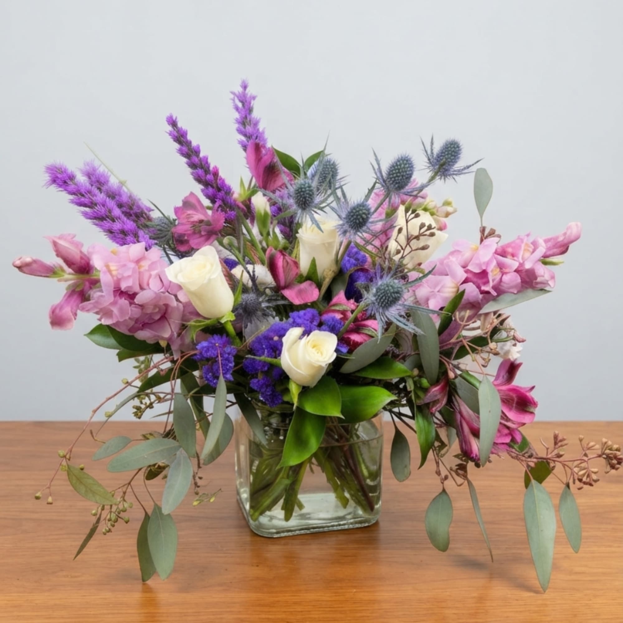 Mixed bouquet of pink, purple, and white flowers in a clear glass vase