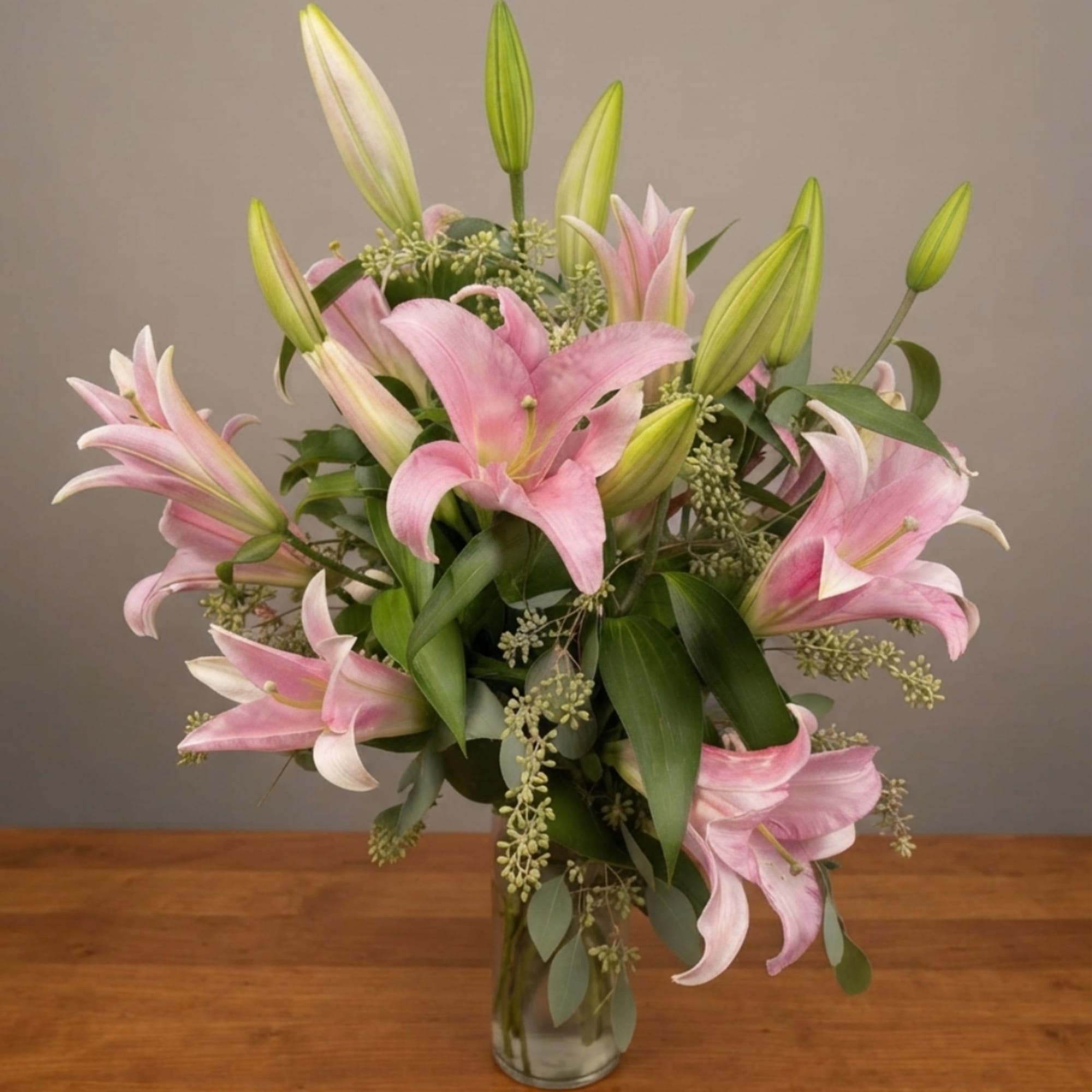 Pink lilies arranged in a clear glass vase with green foliage