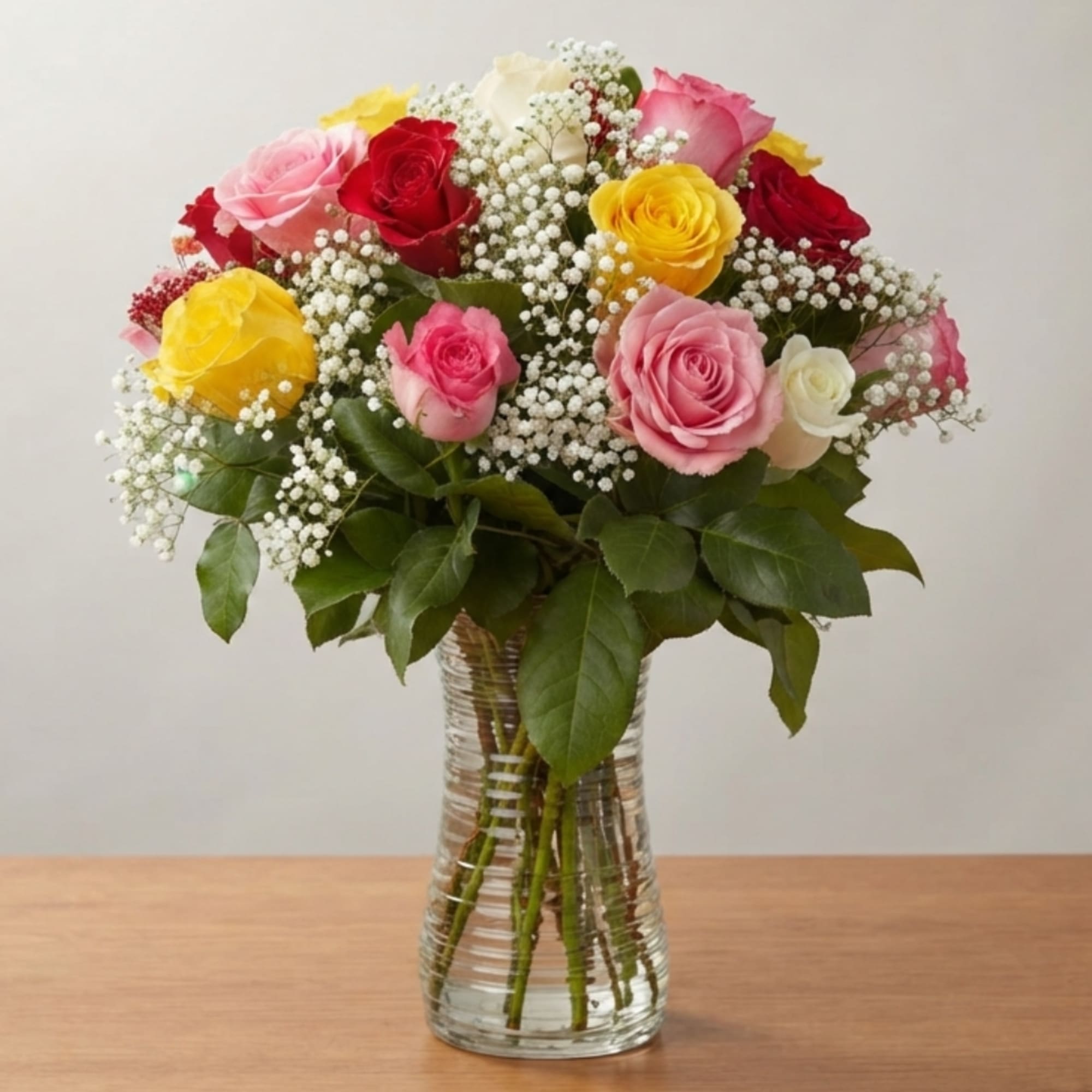 Mixed roses in pink, red, and yellow arranged in a clear glass vase