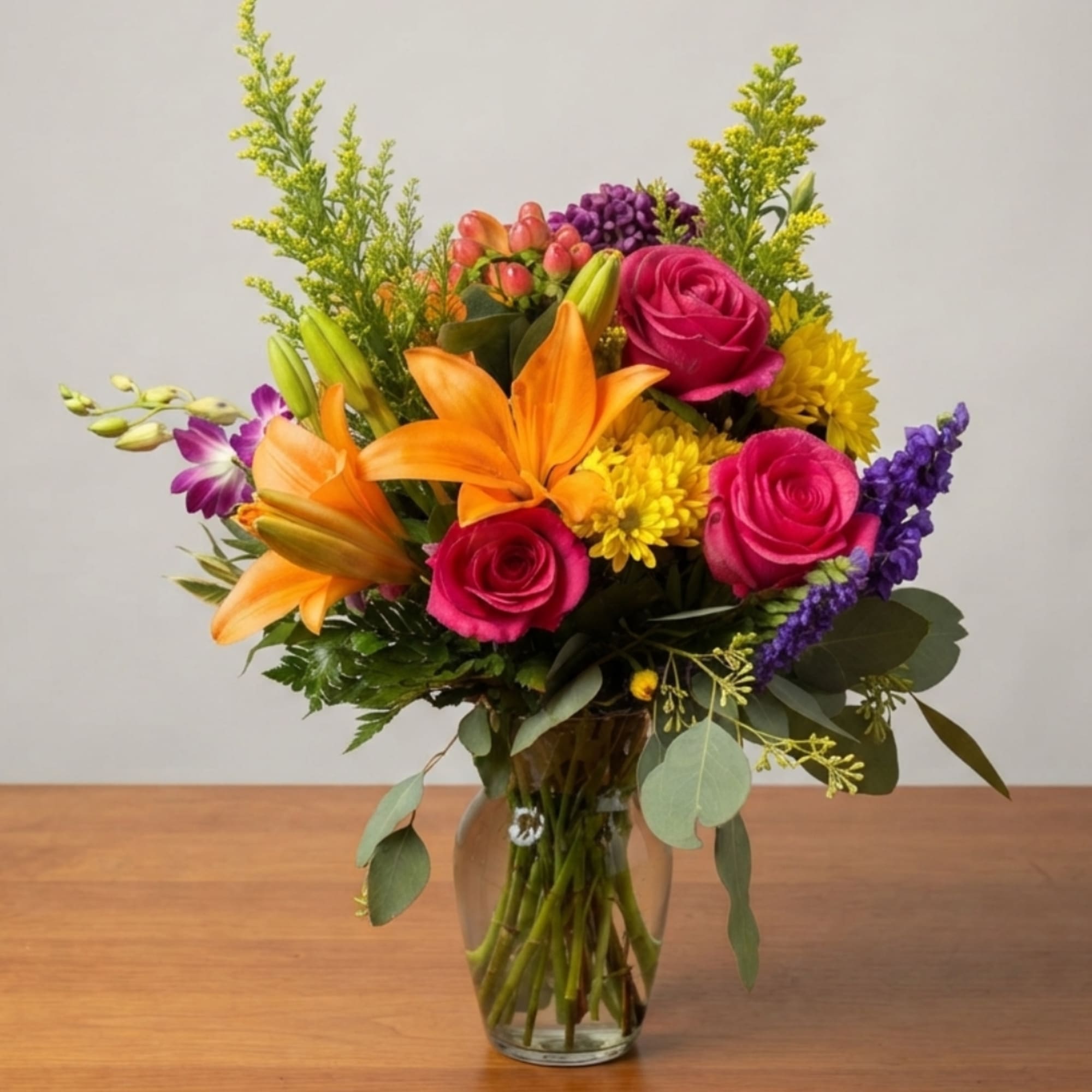 Mixed bouquet of roses, lilies, and purple flowers in a glass vase