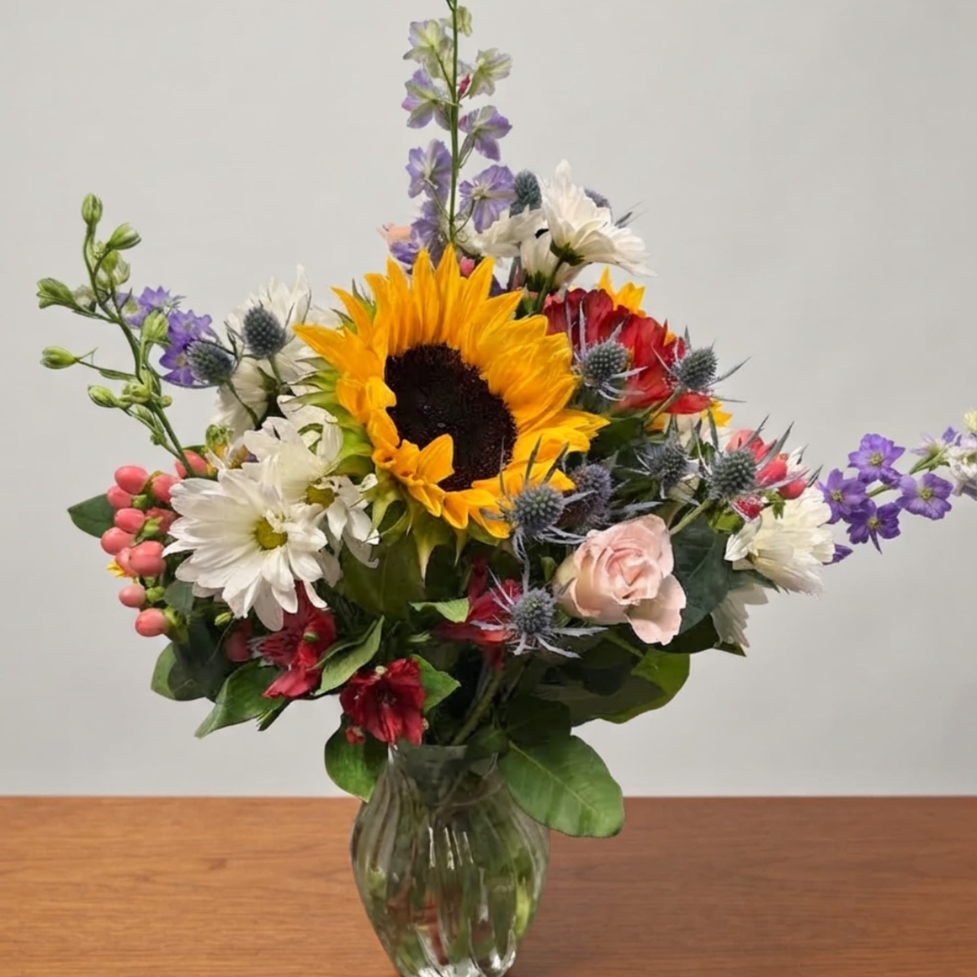 Mixed bouquet with a sunflower, daisies, and roses in a glass vase