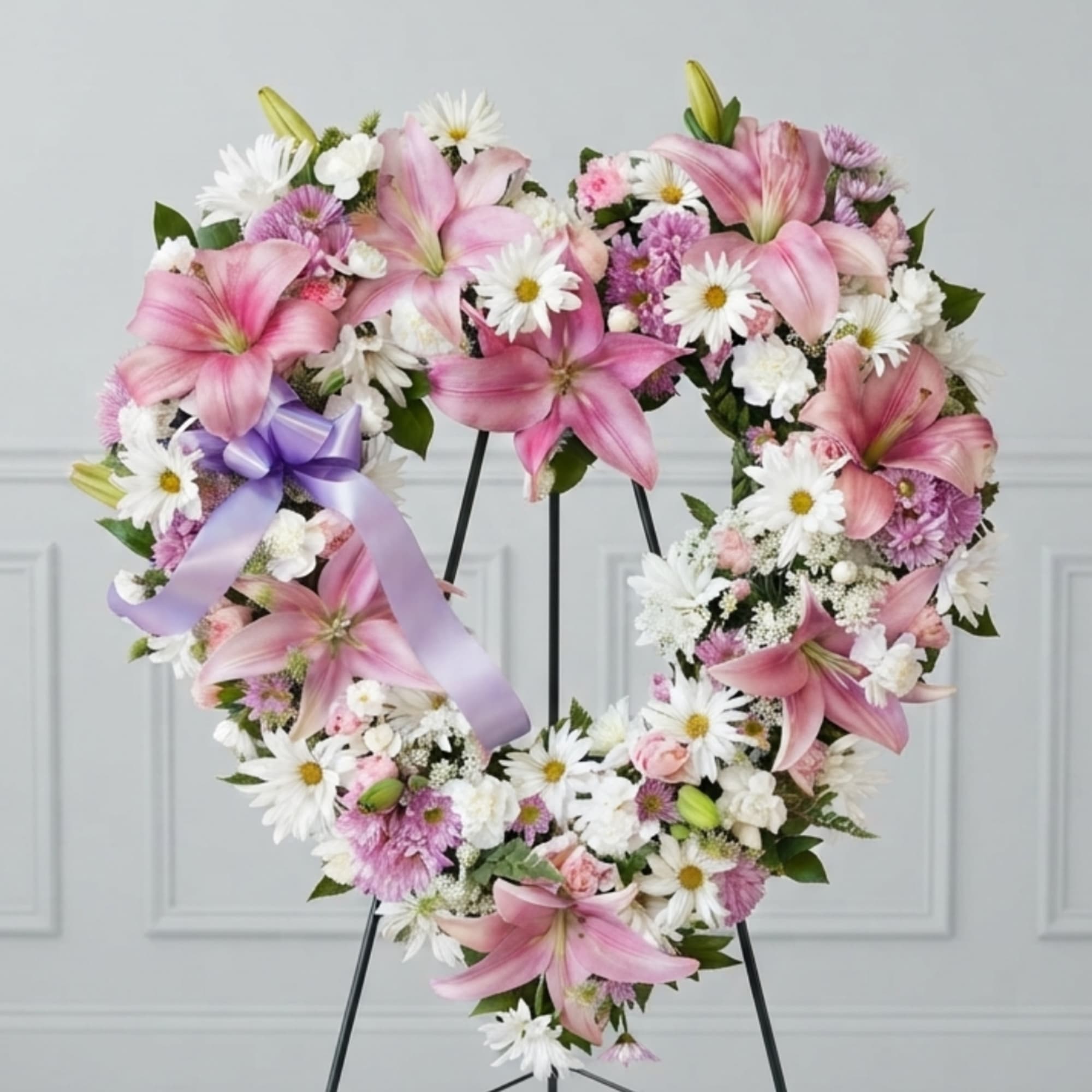 Heart-shaped floral wreath with pink lilies, white daisies, and a lavender ribbon