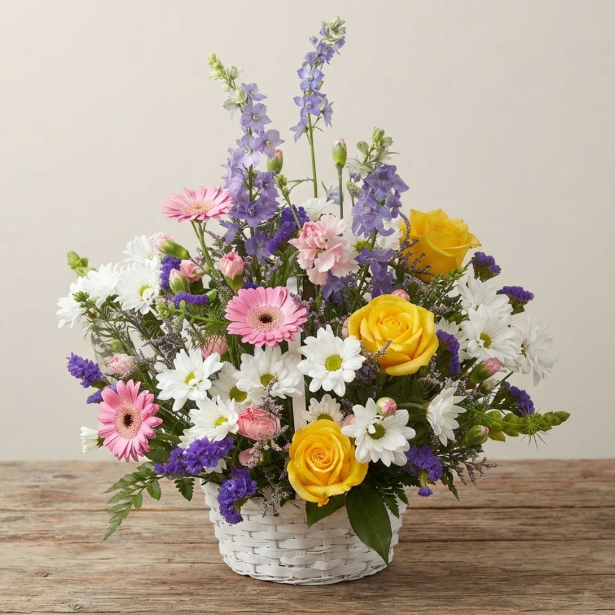 Mixed bouquet in a white basket with yellow roses, pink gerberas, and white daisies