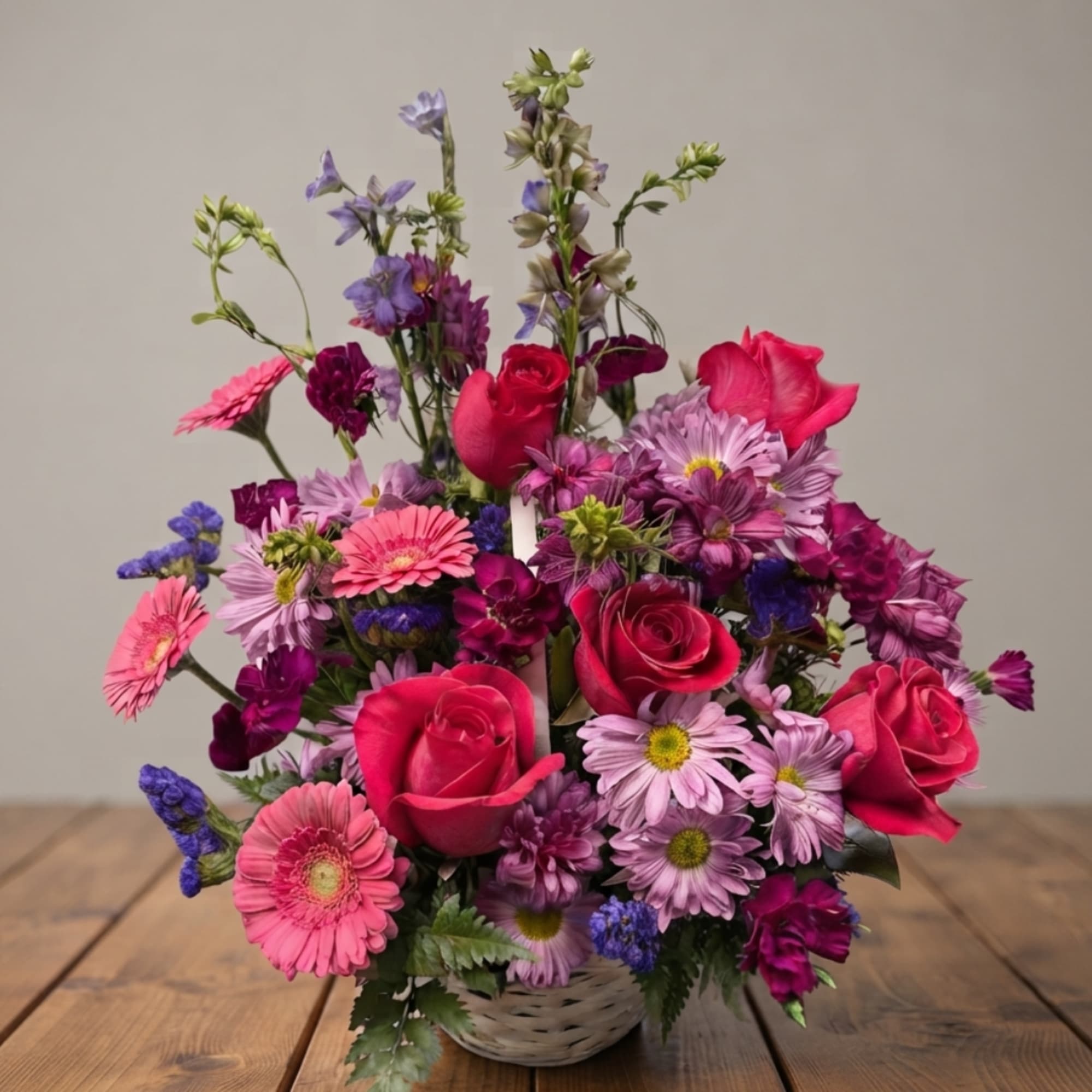 Mixed pink, purple, and red flowers arranged in a white basket.
