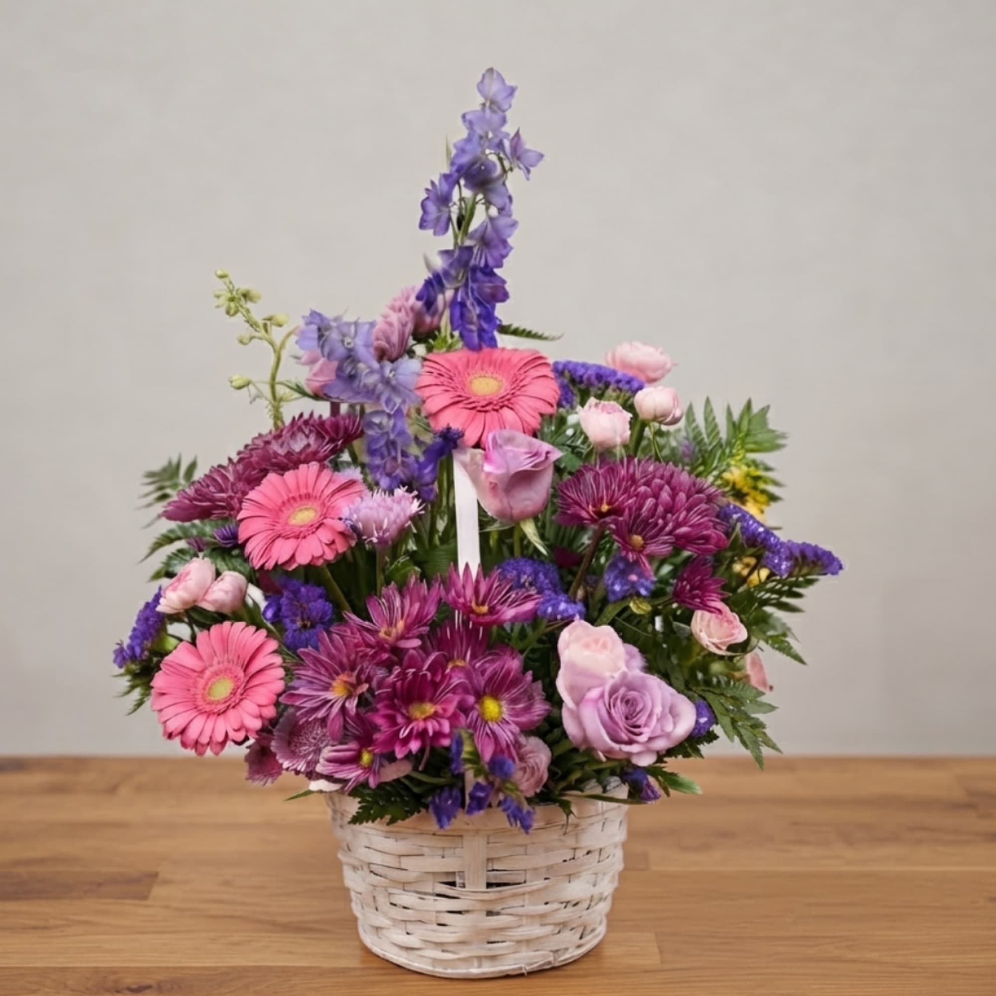 Pink and purple mixed flower arrangement in a white wicker basket