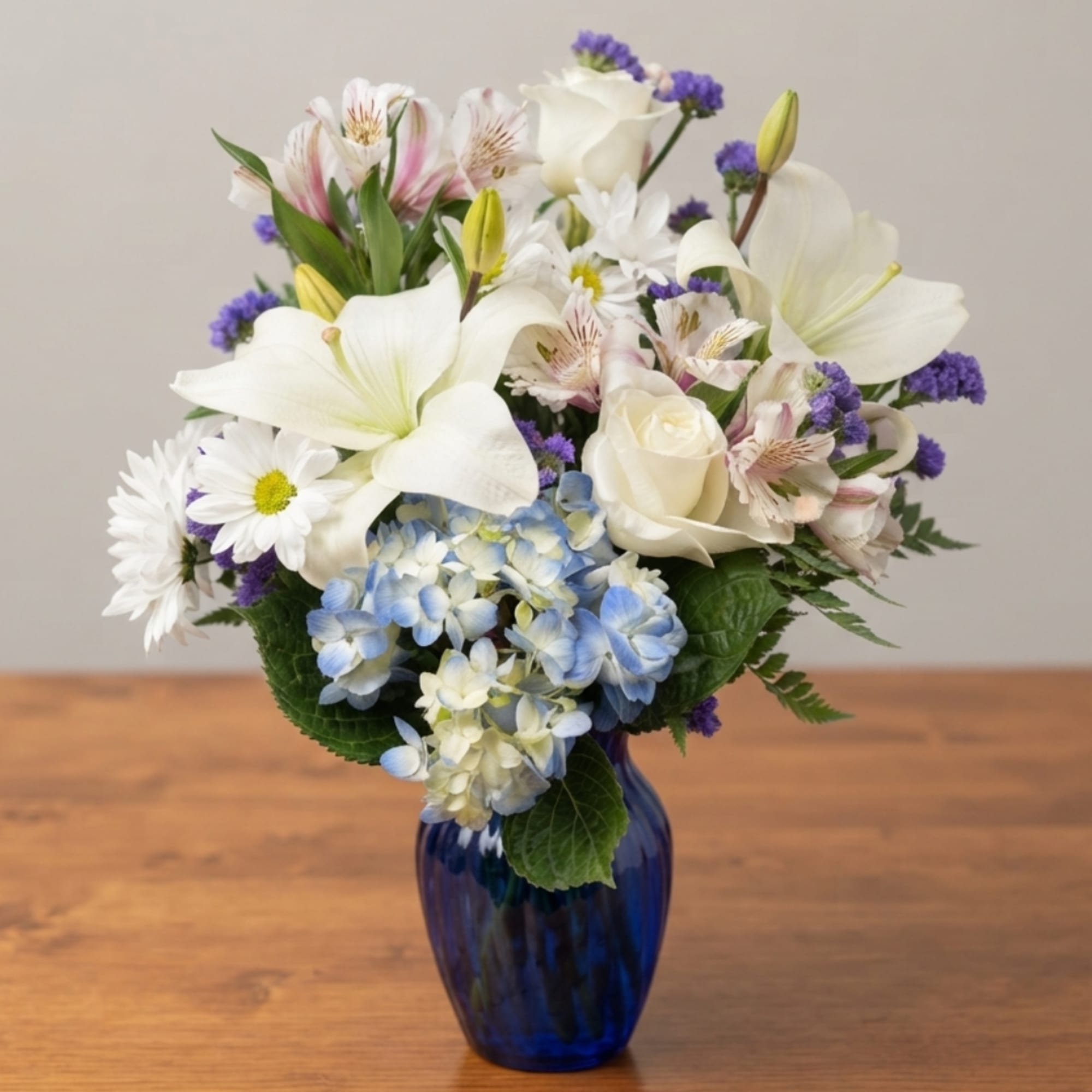 White lilies, roses, and blue hydrangeas in a blue vase