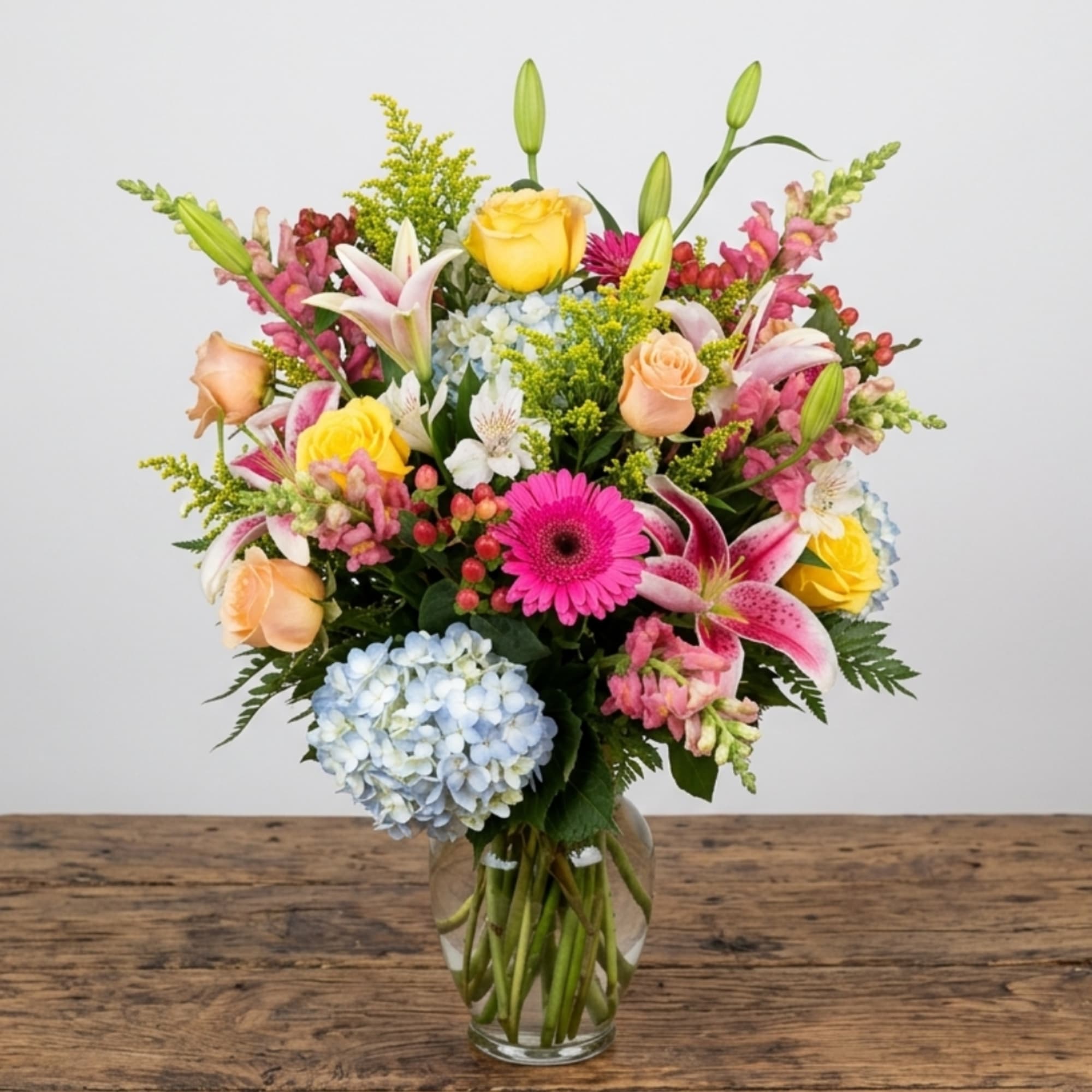 Mixed bouquet of lilies, roses, gerbera daisies, and hydrangea in a glass vase