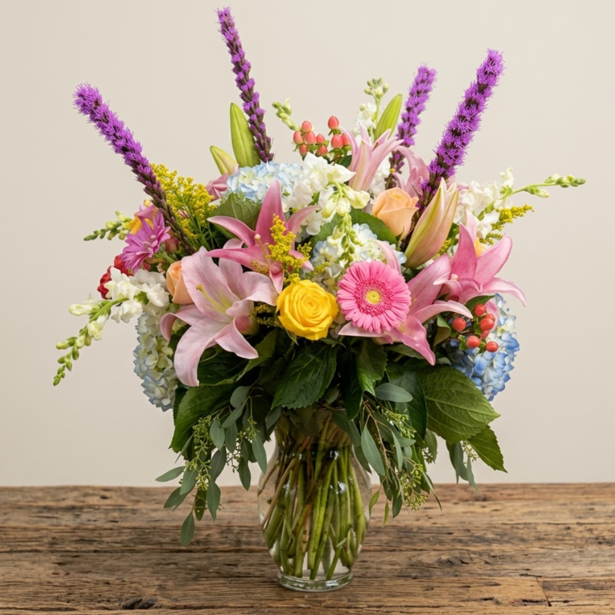 Mixed bouquet of pink lilies, roses, and daisies in a glass vase