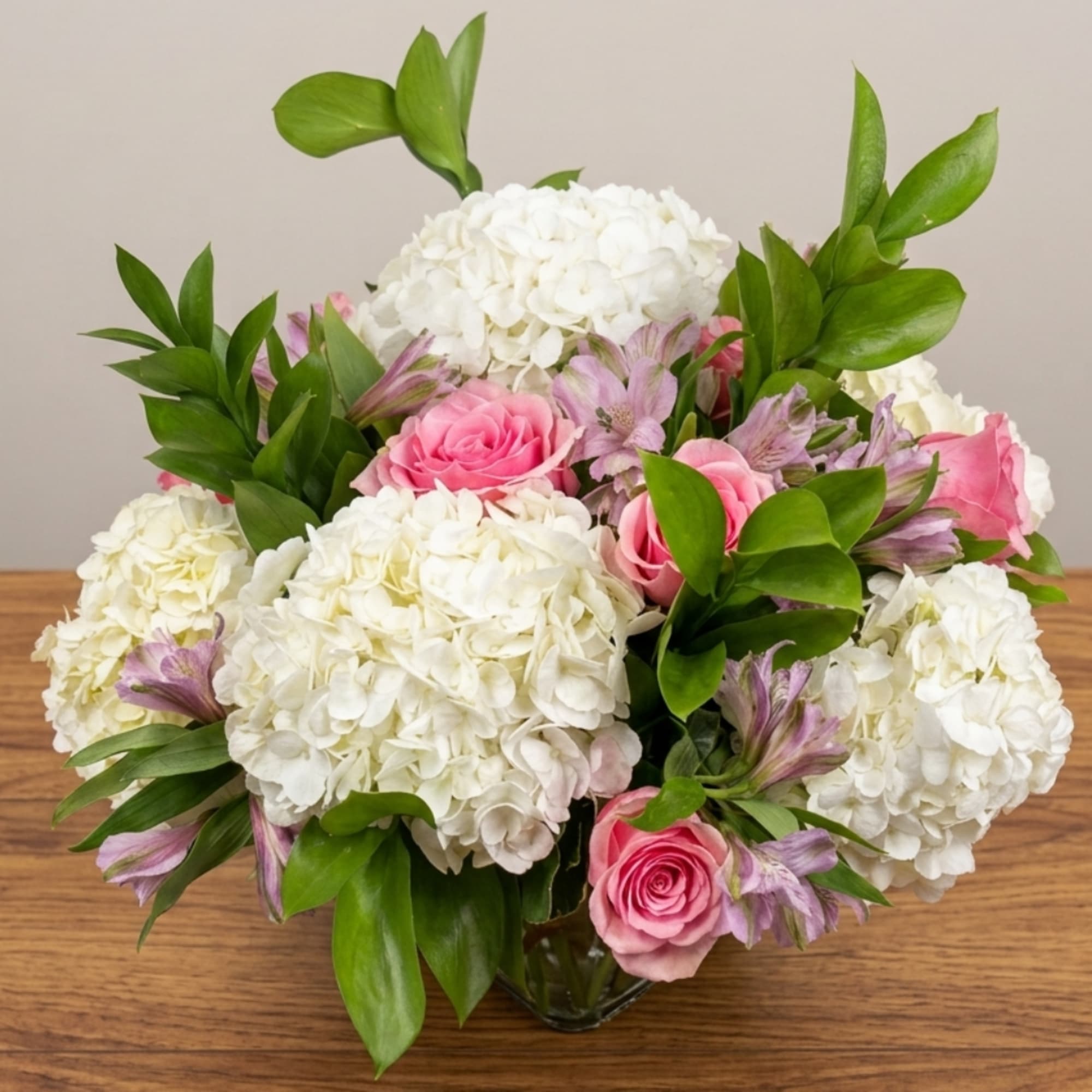 Pink roses and white hydrangeas in a glass vase with purple accents
