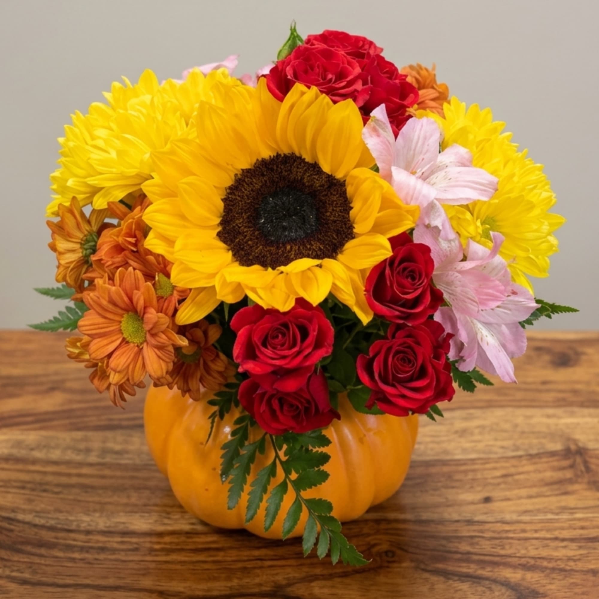 Mixed bouquet in a pumpkin vase with sunflowers, roses, and mums