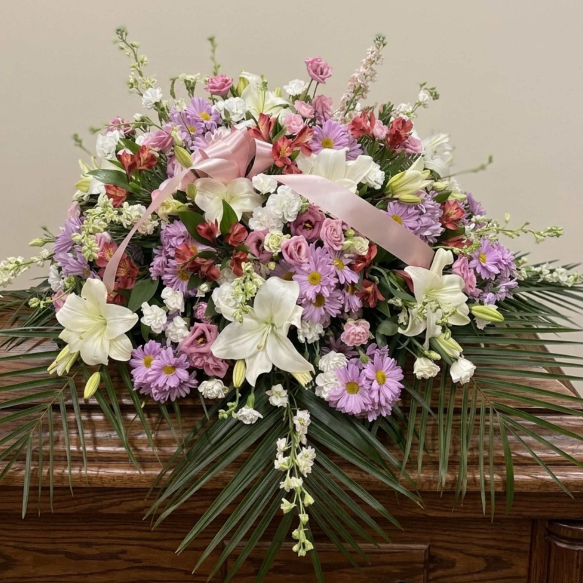 Large pastel floral arrangement with lilies, daisies, and a pink ribbon