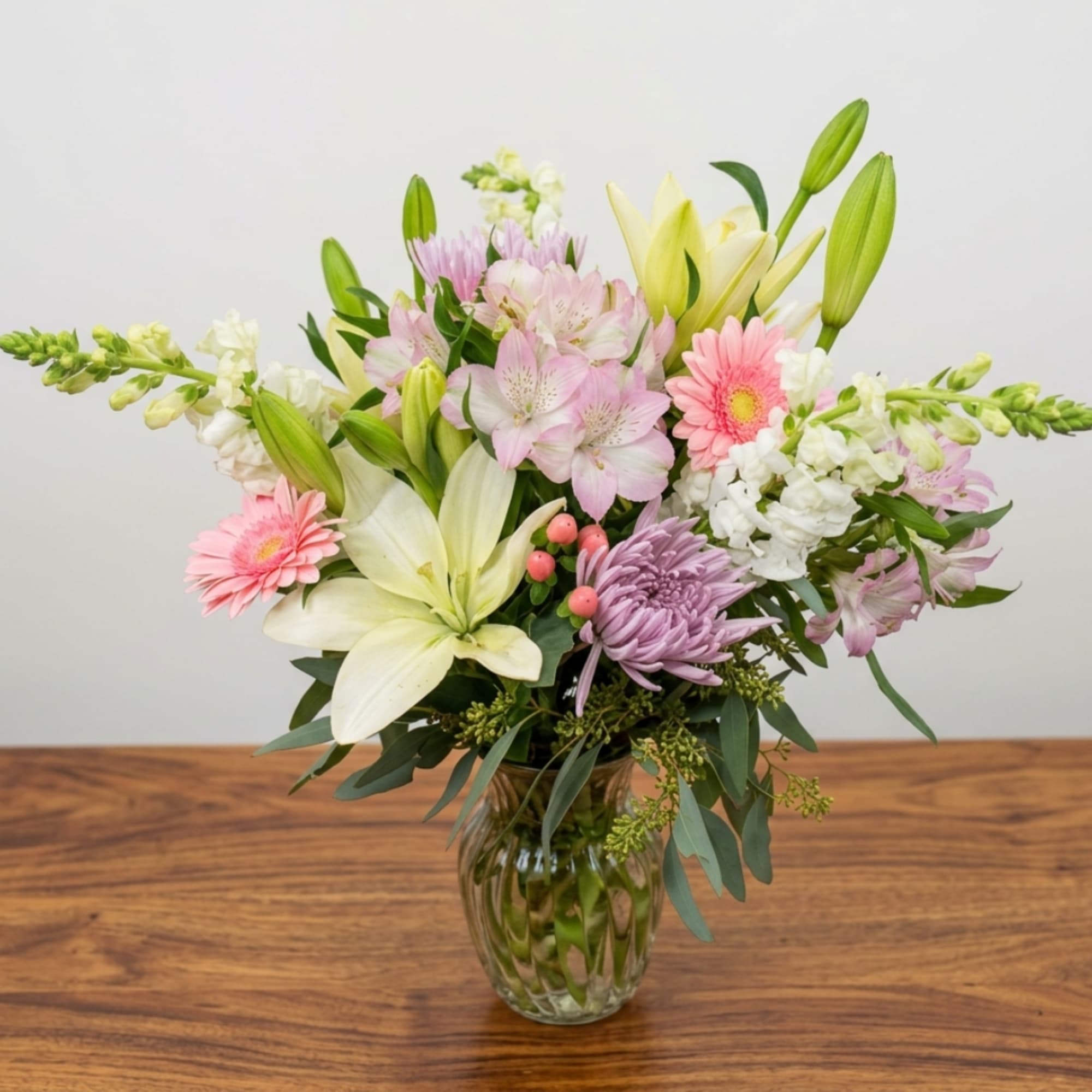 Mixed bouquet of lilies, gerbera daisies, and pastel flowers in a glass vase