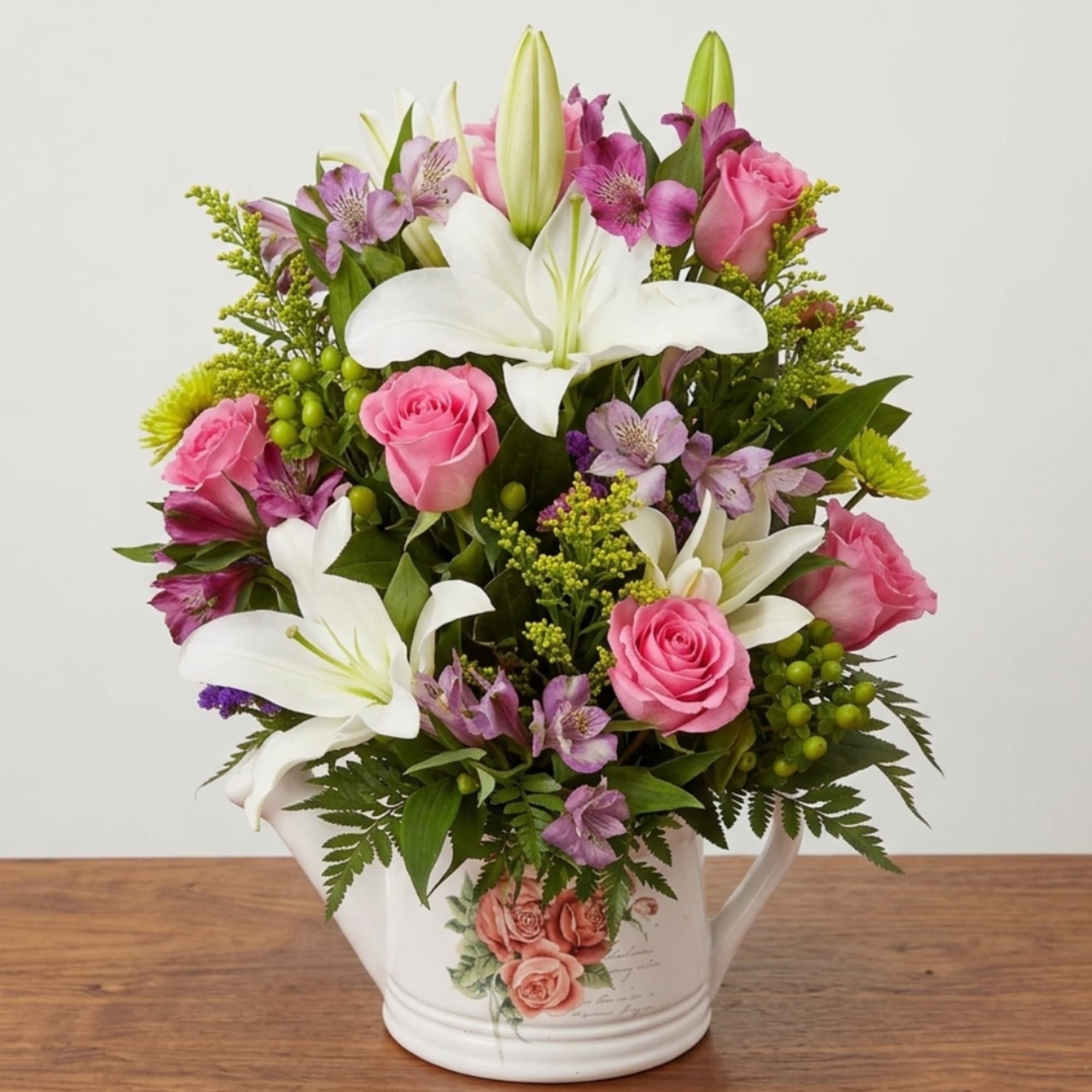 Pink roses and white lilies arranged in a white watering can vase