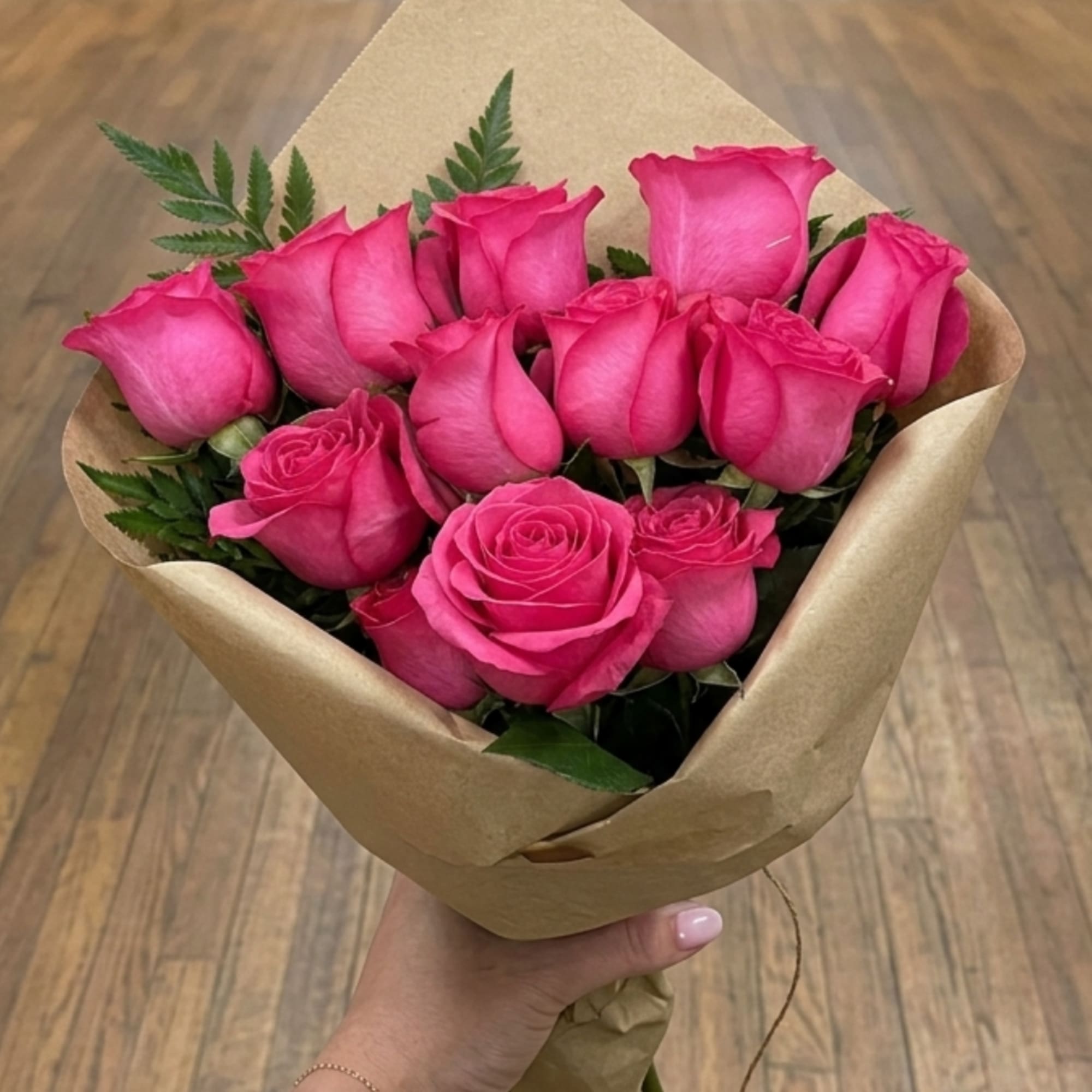 Handheld bouquet of bright pink roses wrapped in brown paper