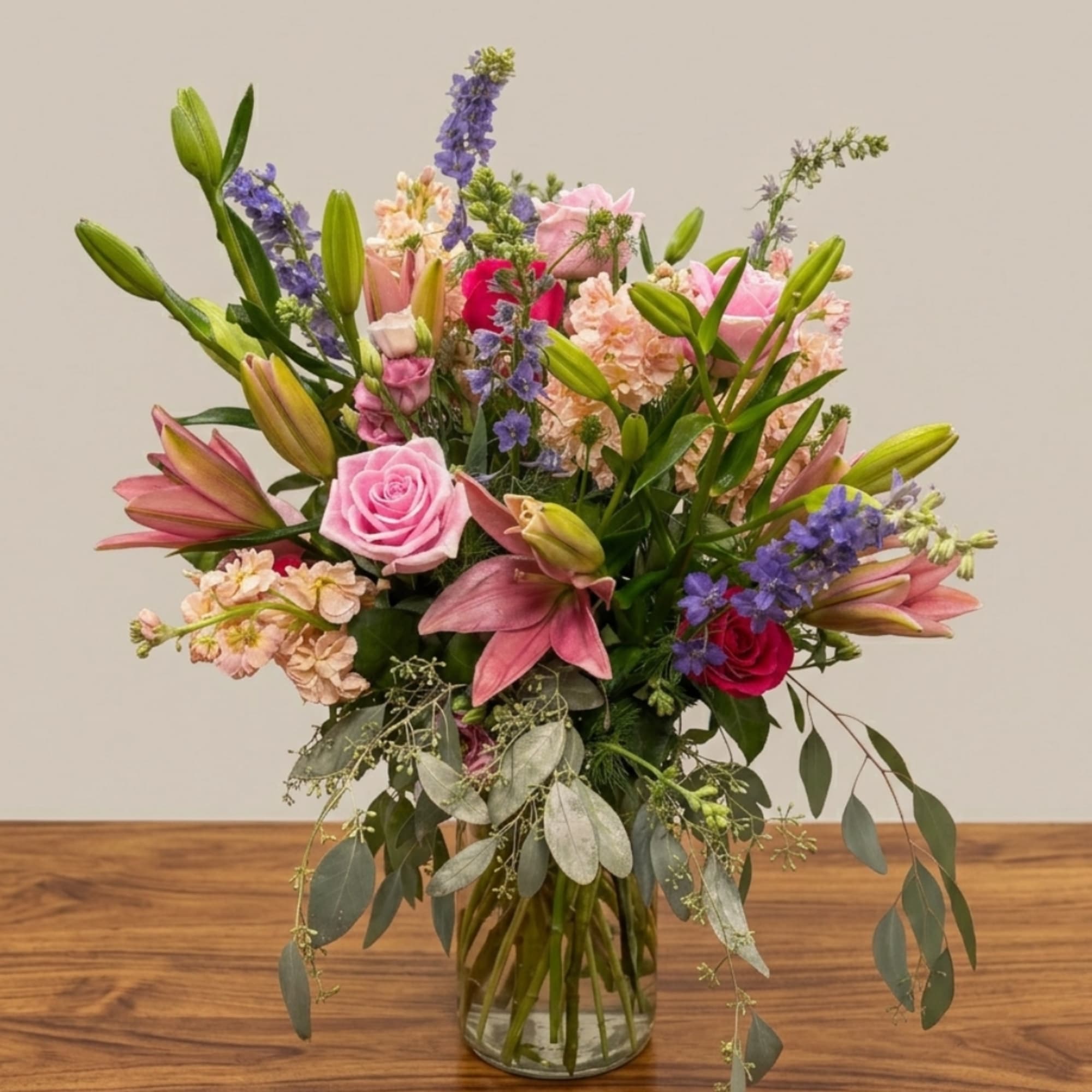 Mixed bouquet of pink roses, lilies, and purple flowers in a glass vase