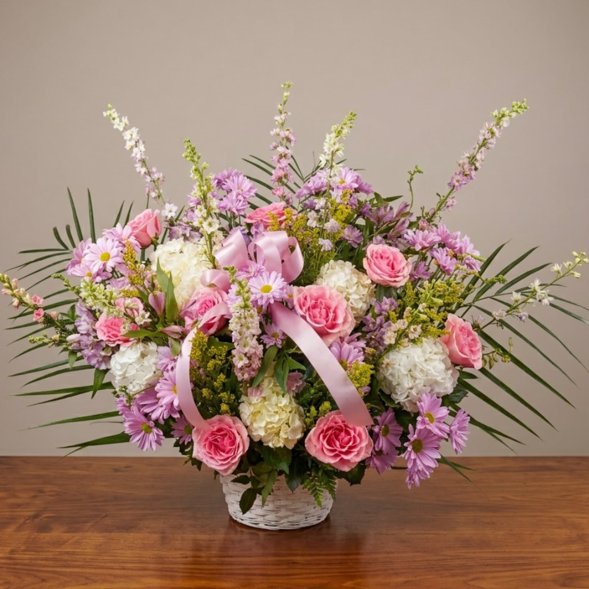 Pink and white flower arrangement in a white basket with a pink ribbon