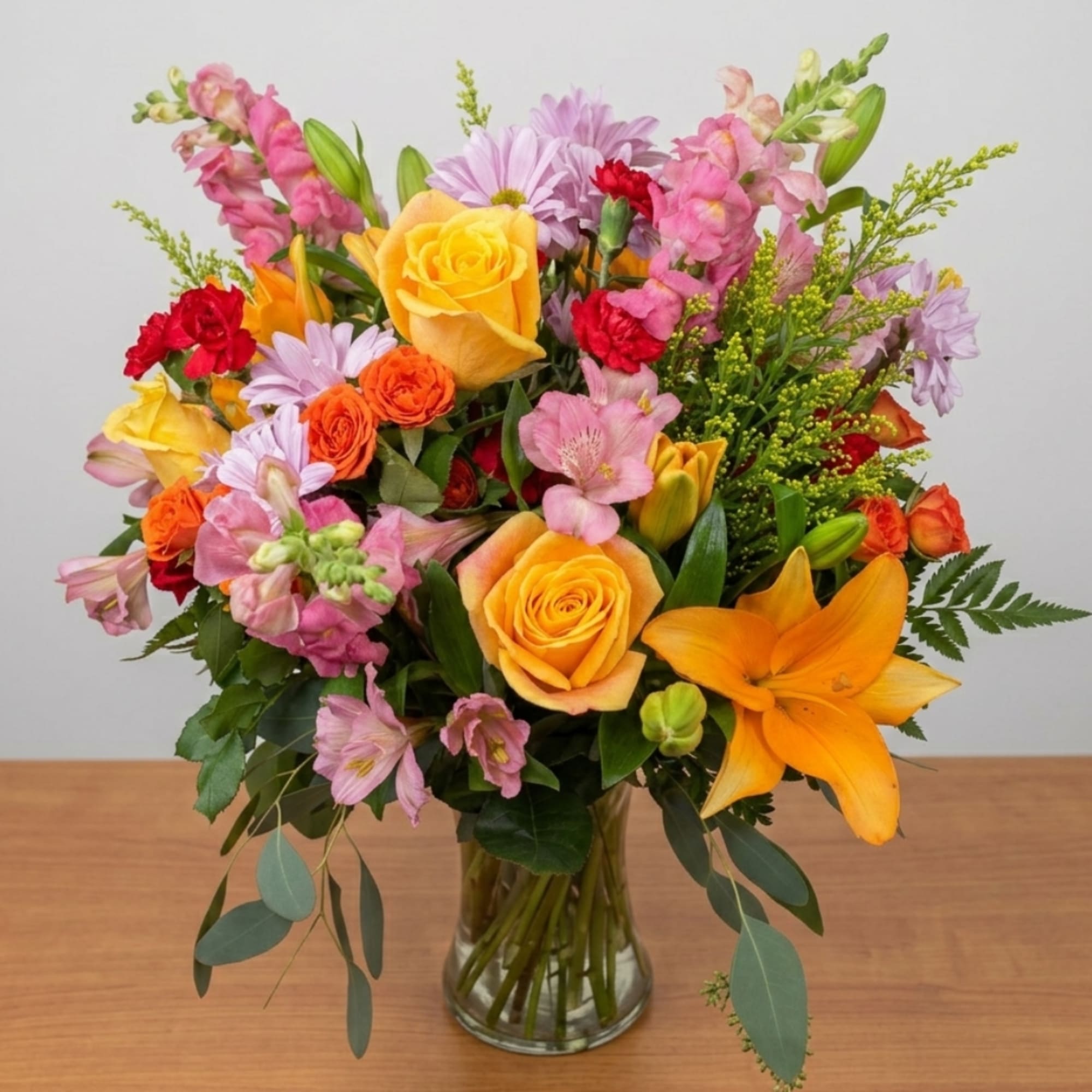 Mixed bouquet of roses, lilies, and pink blooms in a glass vase
