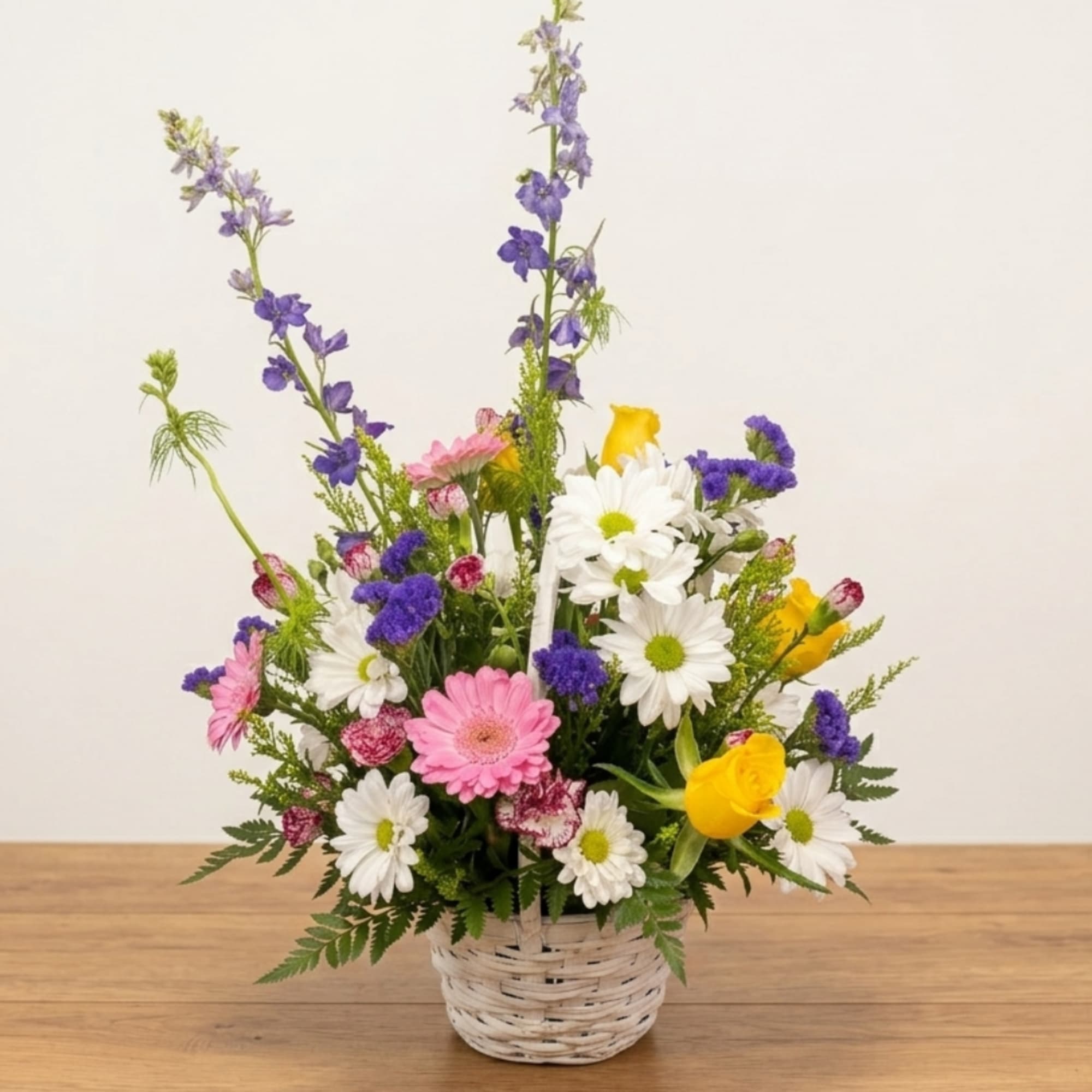 Mixed bouquet in a white wicker basket with daisies, pink blooms, and yellow roses