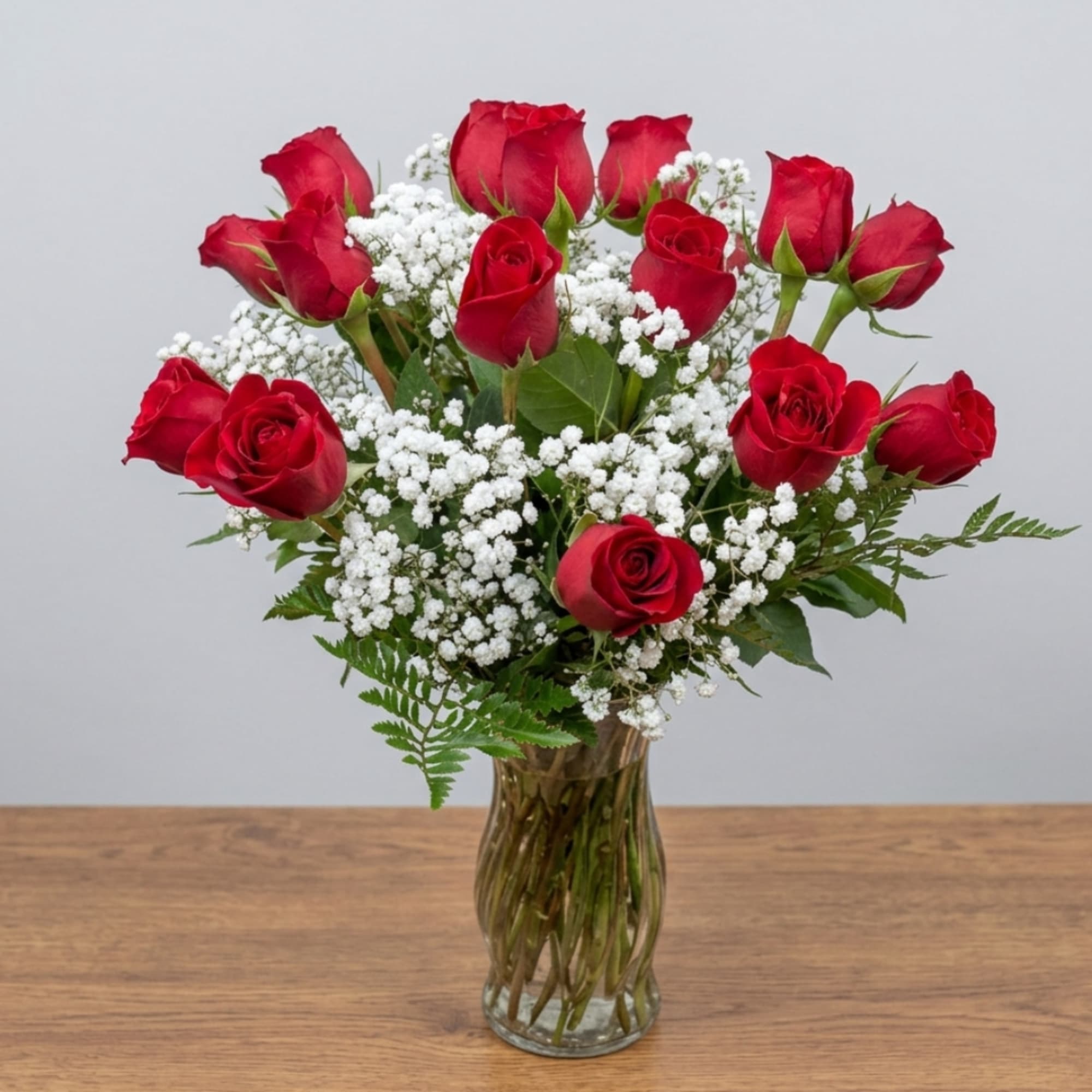 Red roses arranged in a clear glass vase with white filler flowers