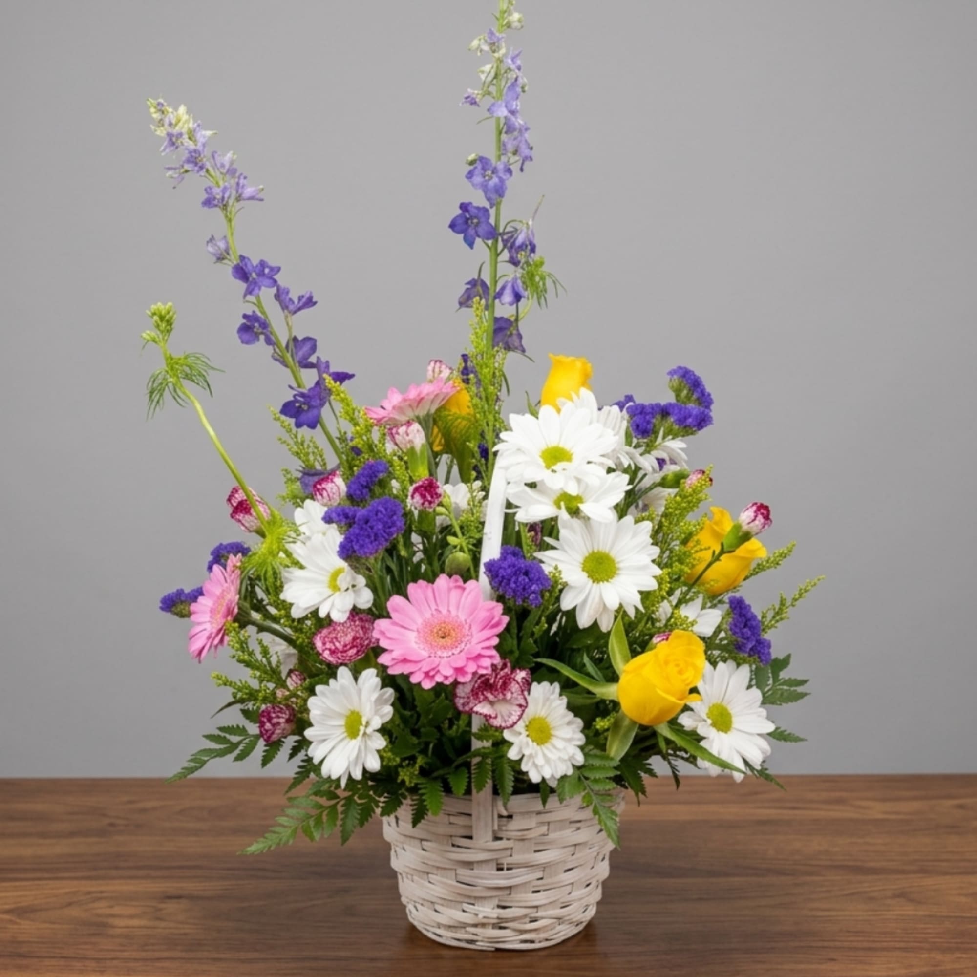 Mixed bouquet in a white wicker basket with daisies, roses, and purple blooms