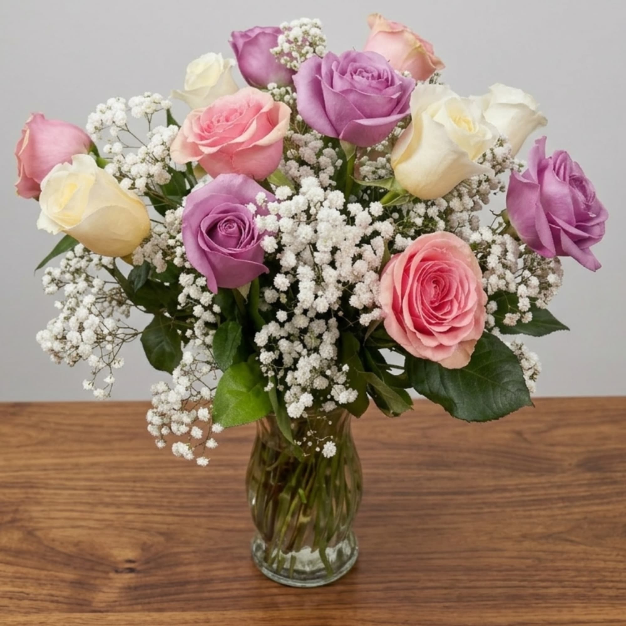 Mixed pink, purple, and white roses in a clear glass vase