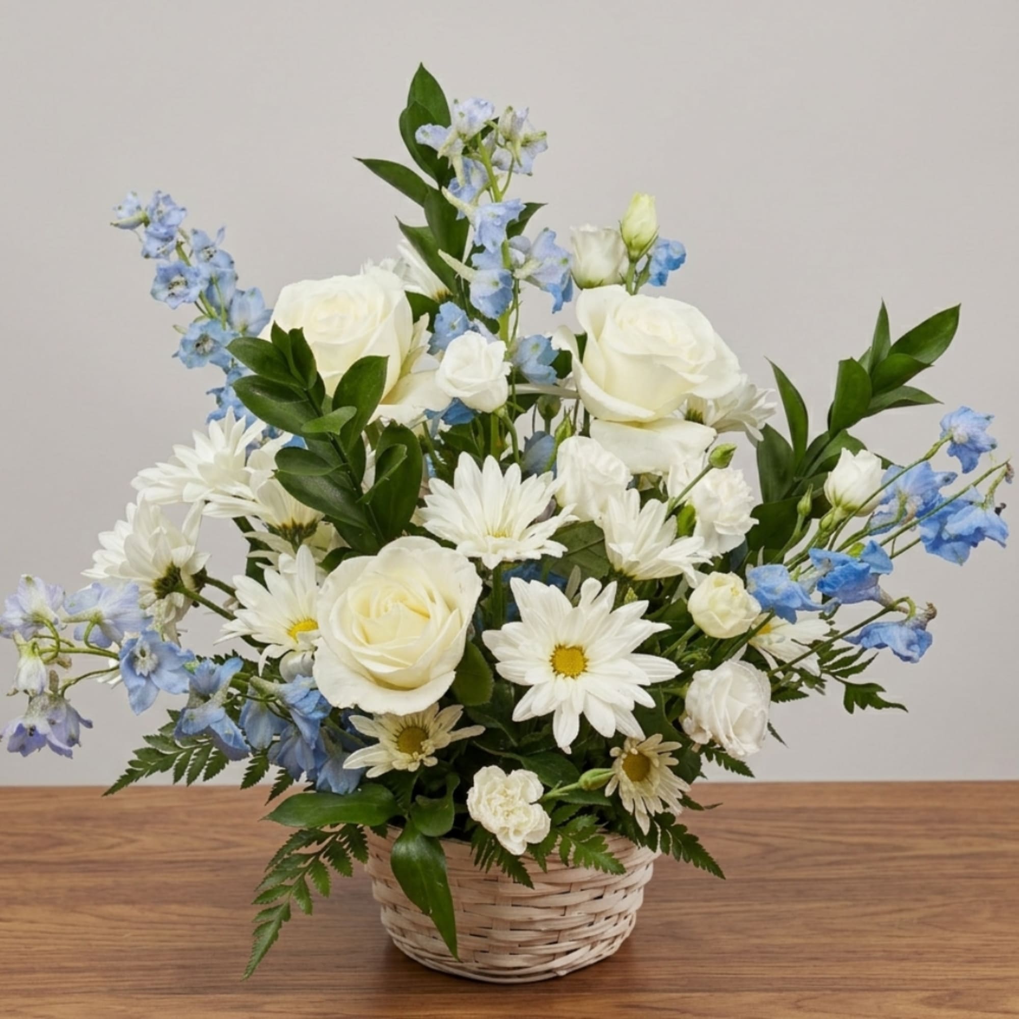 White roses and daisies with blue flowers in a wicker basket