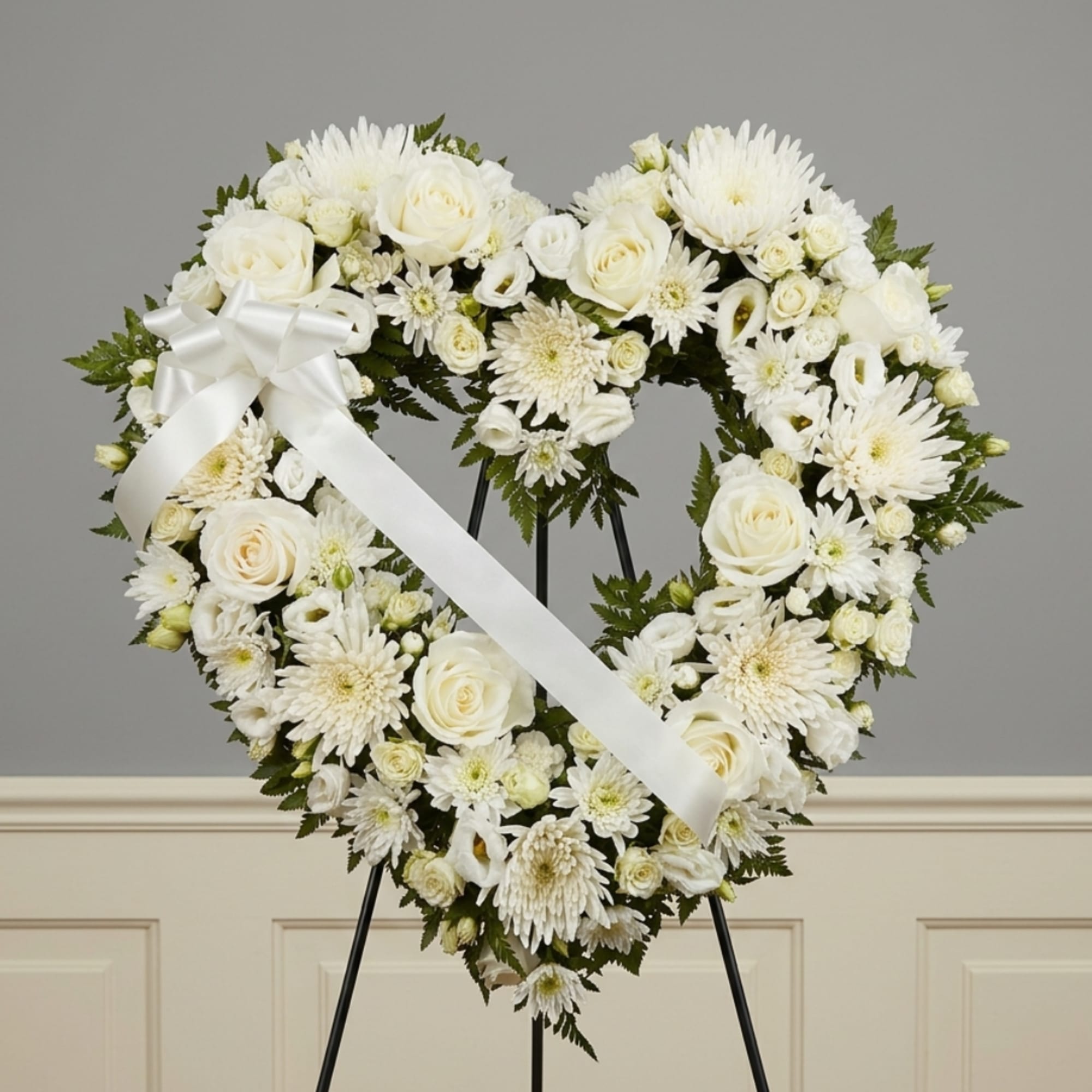Heart-shaped white floral wreath on an easel with a white ribbon bow