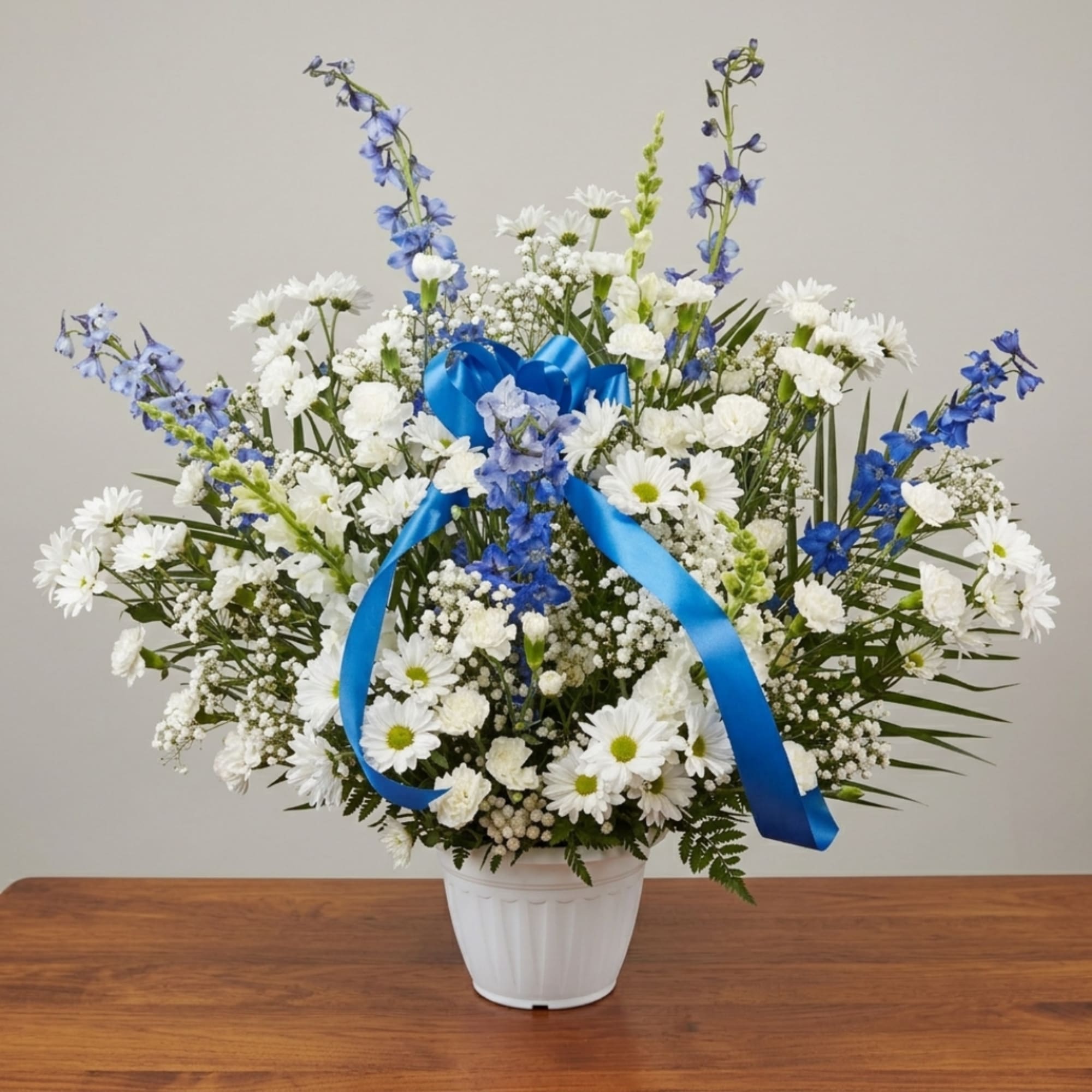 White daisies and blue flowers in a white pot with a blue ribbon