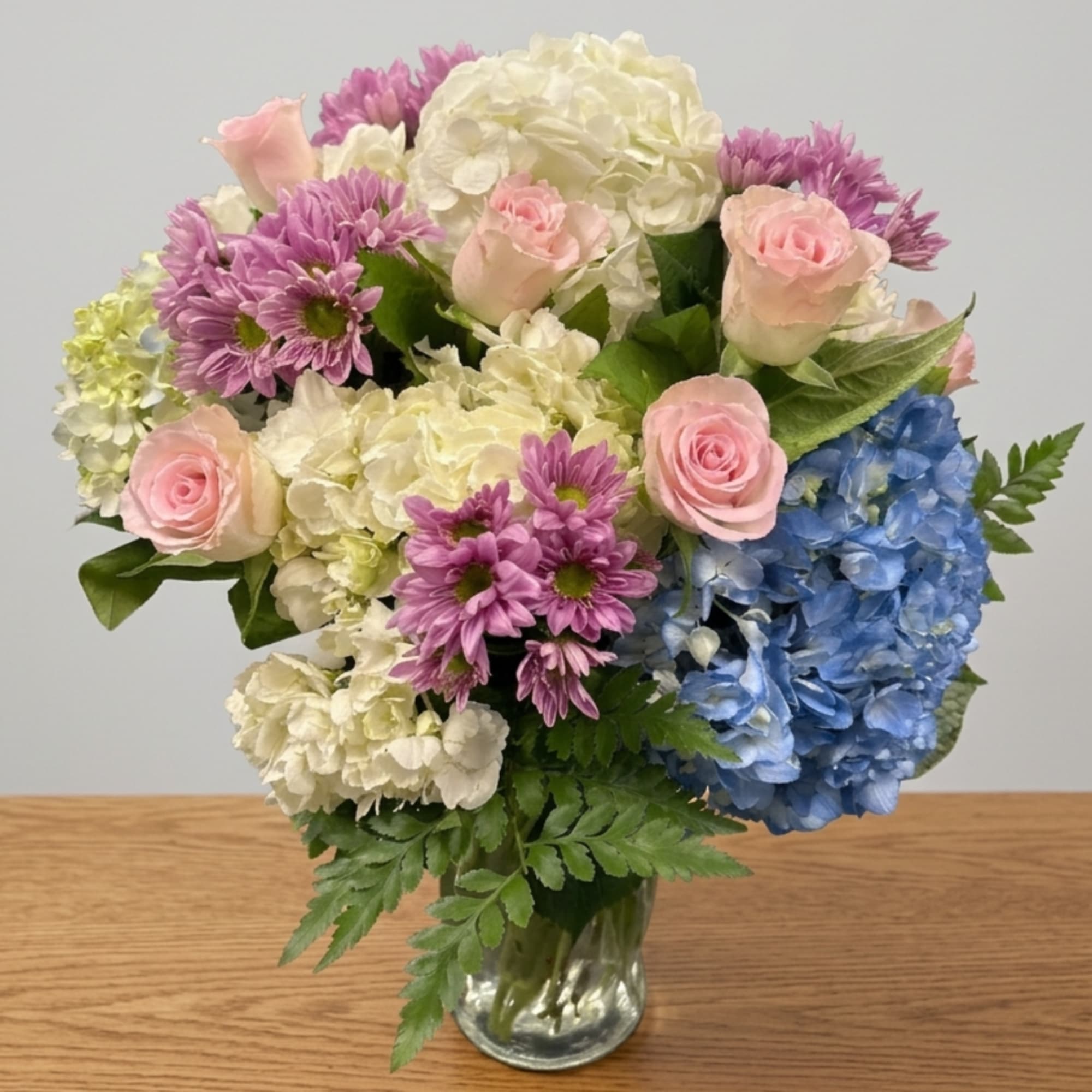 Pink roses and purple daisies with hydrangeas in a clear glass vase