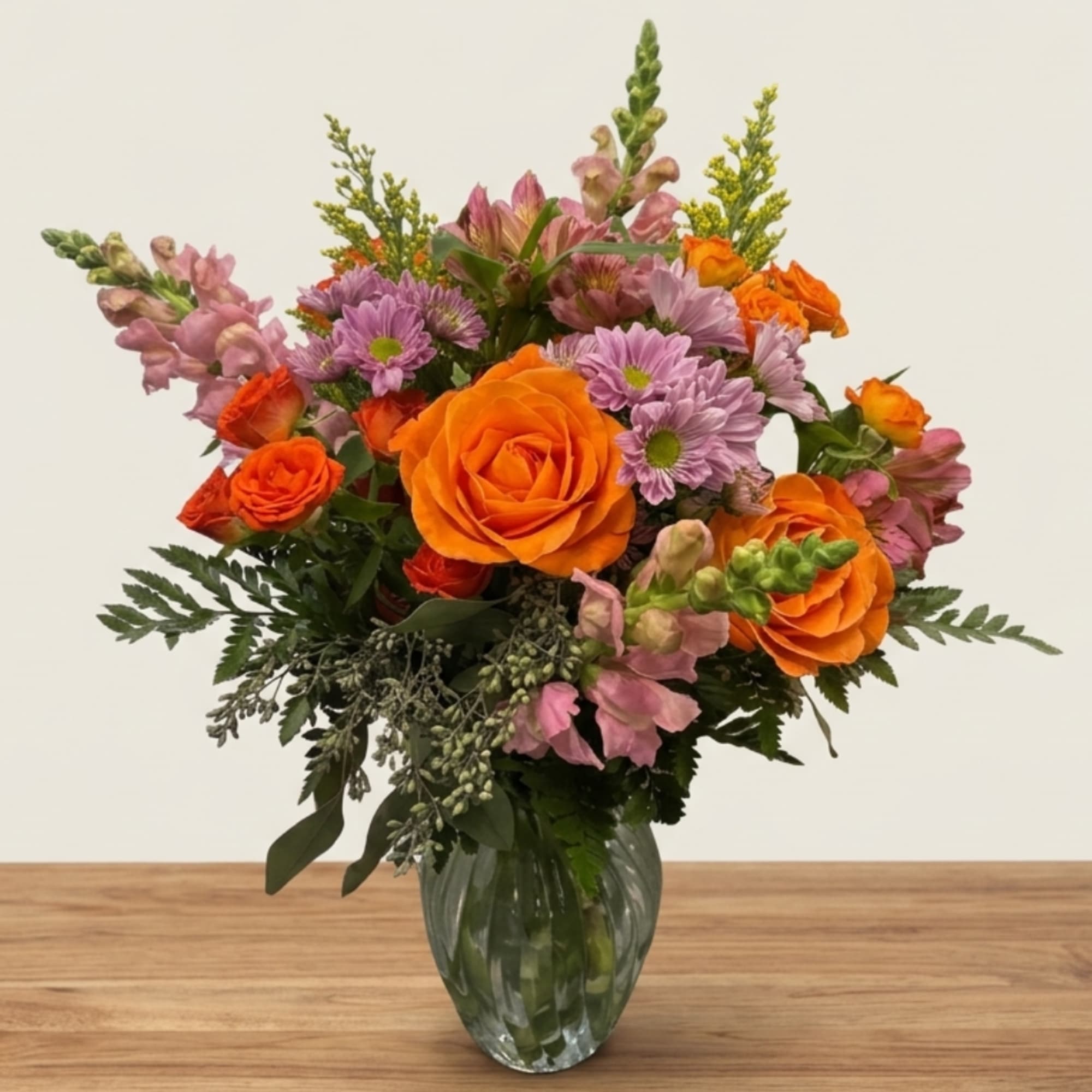 Orange roses and lavender daisies in a clear glass vase