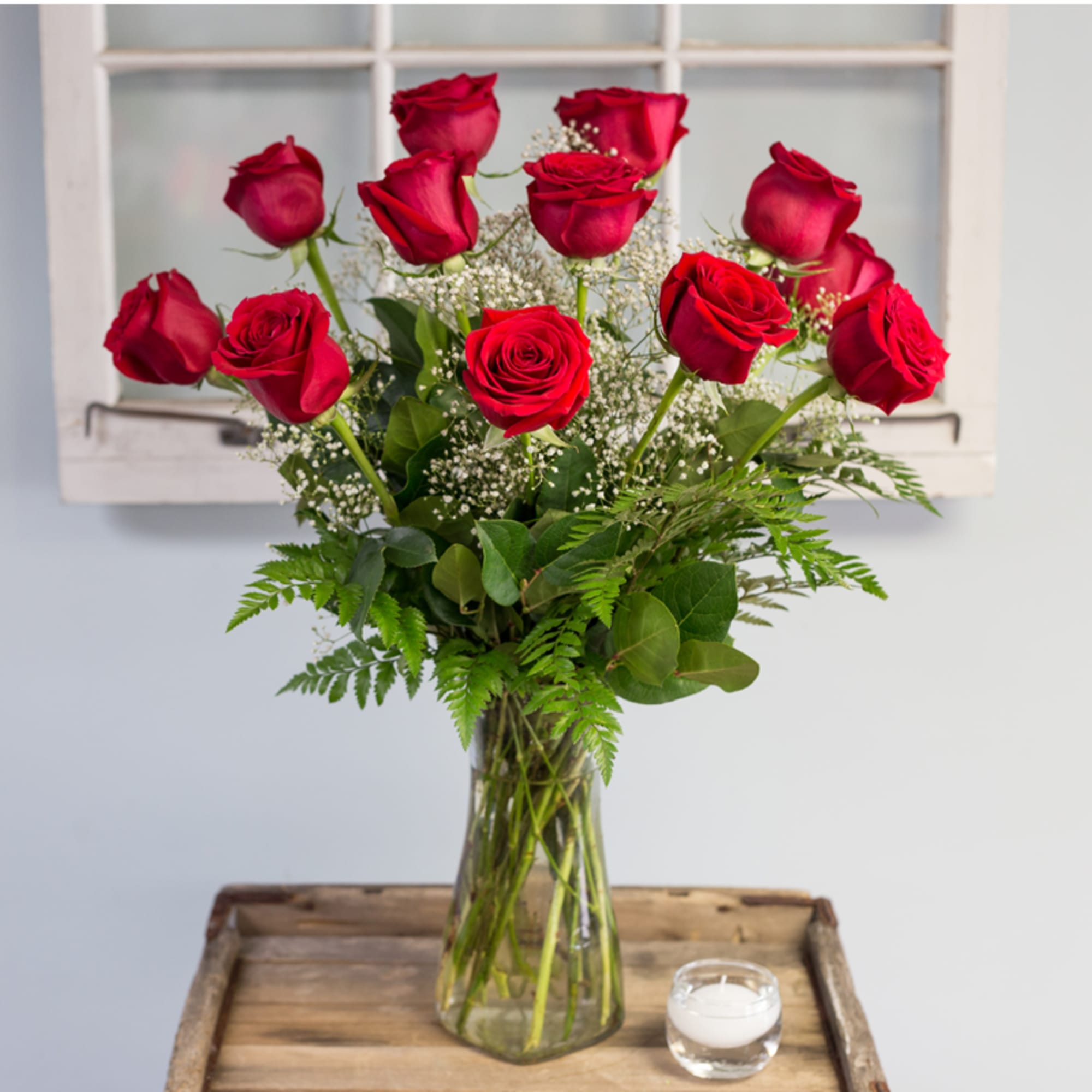 Red roses in a clear glass vase with baby's breath and greenery